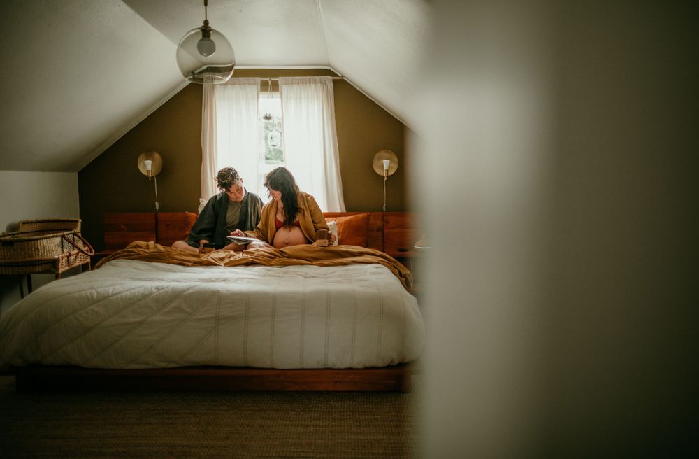 queer couple does crossword puzzle in bed maternity photography session portland oregon