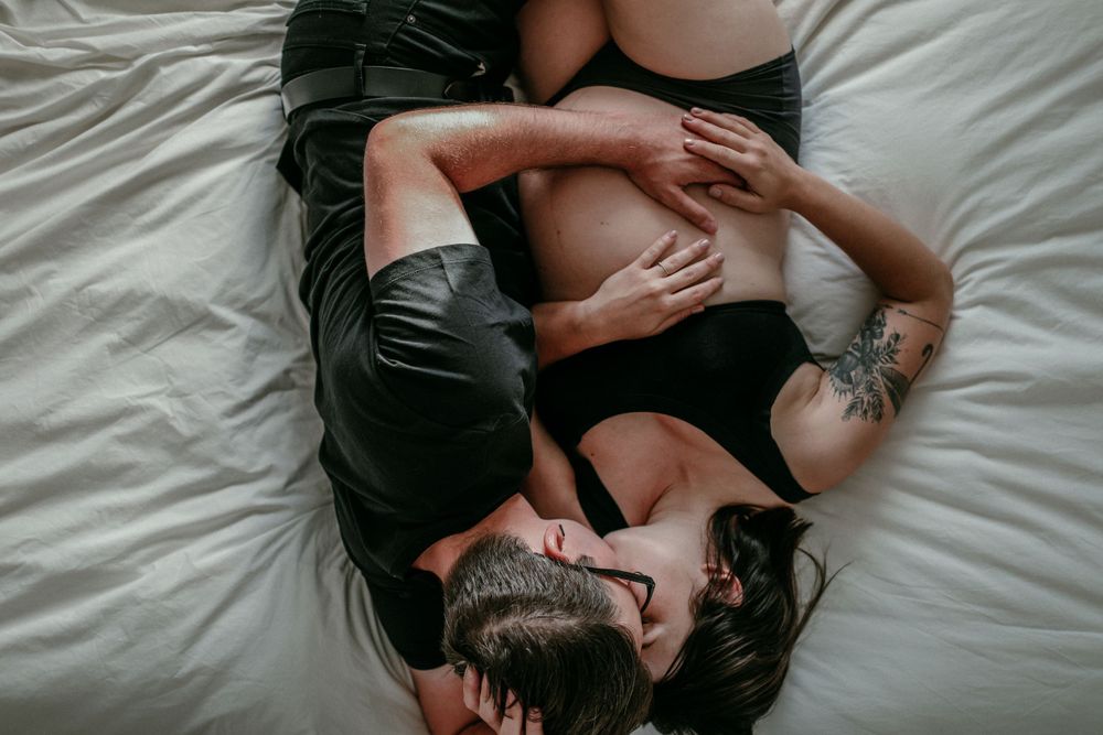 in home maternity session couple embraces on bed pov from above documentary photographer portland oregon
