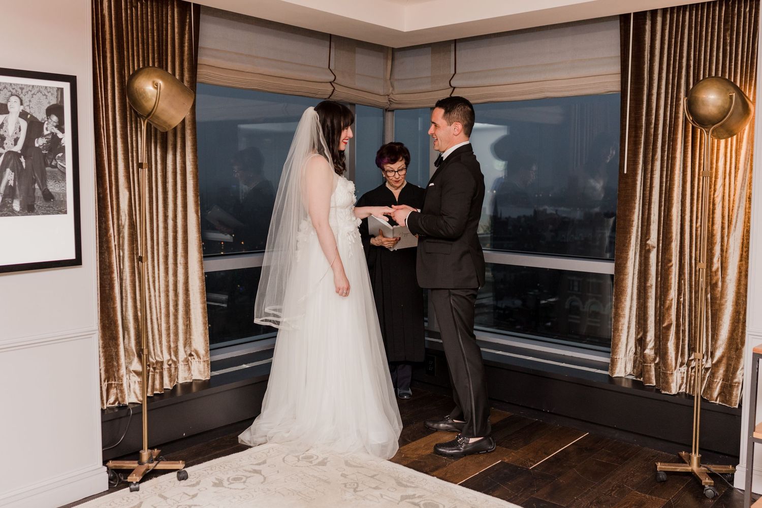 A couple stands in their wedding attire during their ceremony in a penthouse suite in the city.