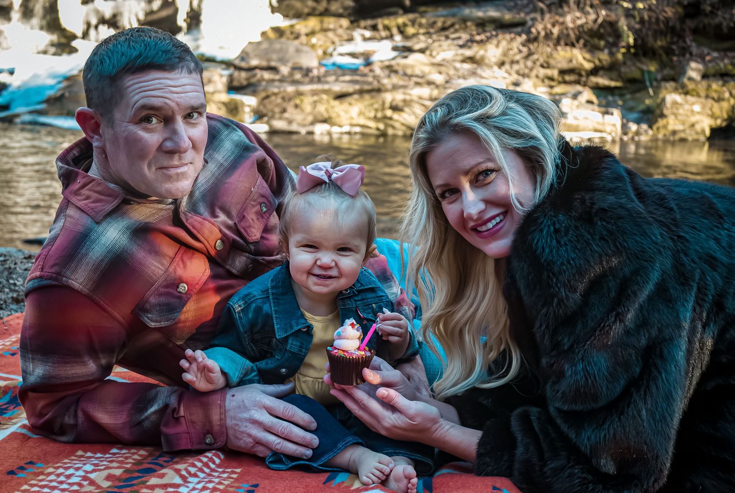 Family enjoying a picnic outdoors on a plaid blanket in autumn setting.