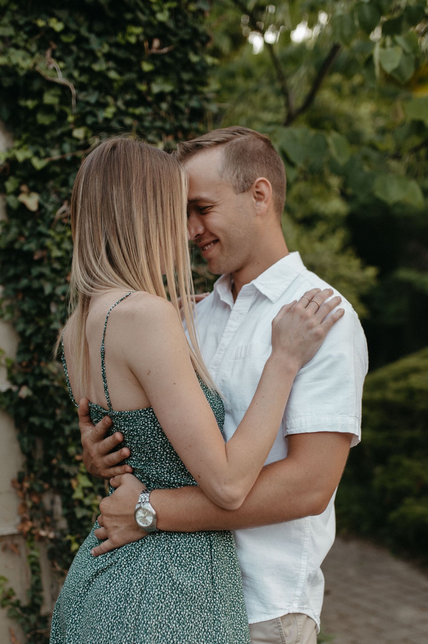 Couple embracing outdoors wearing coordinated summer outfits against greenery background.
