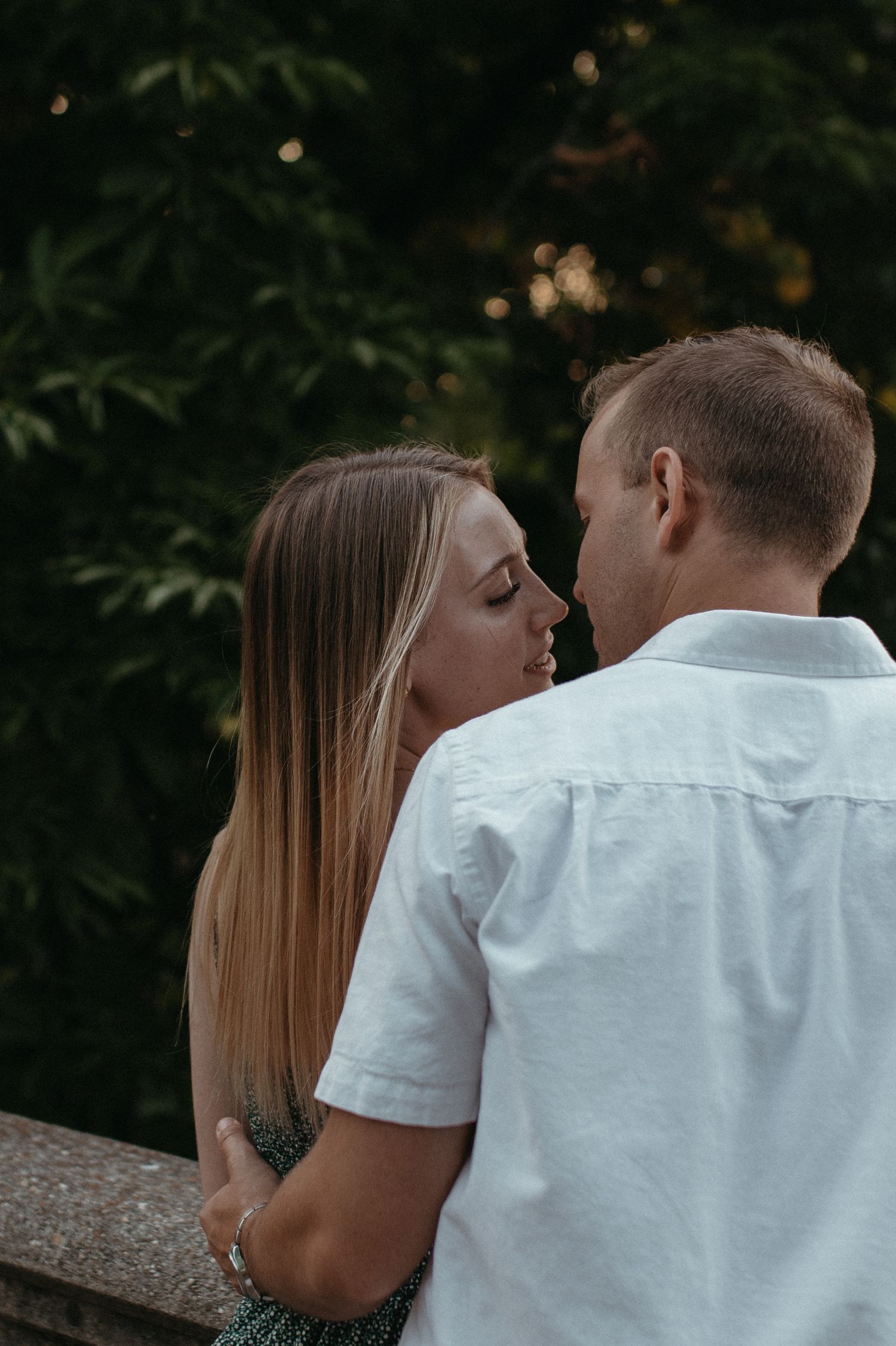 Intimate moment between couple on stone overlook with leafy trees in background.