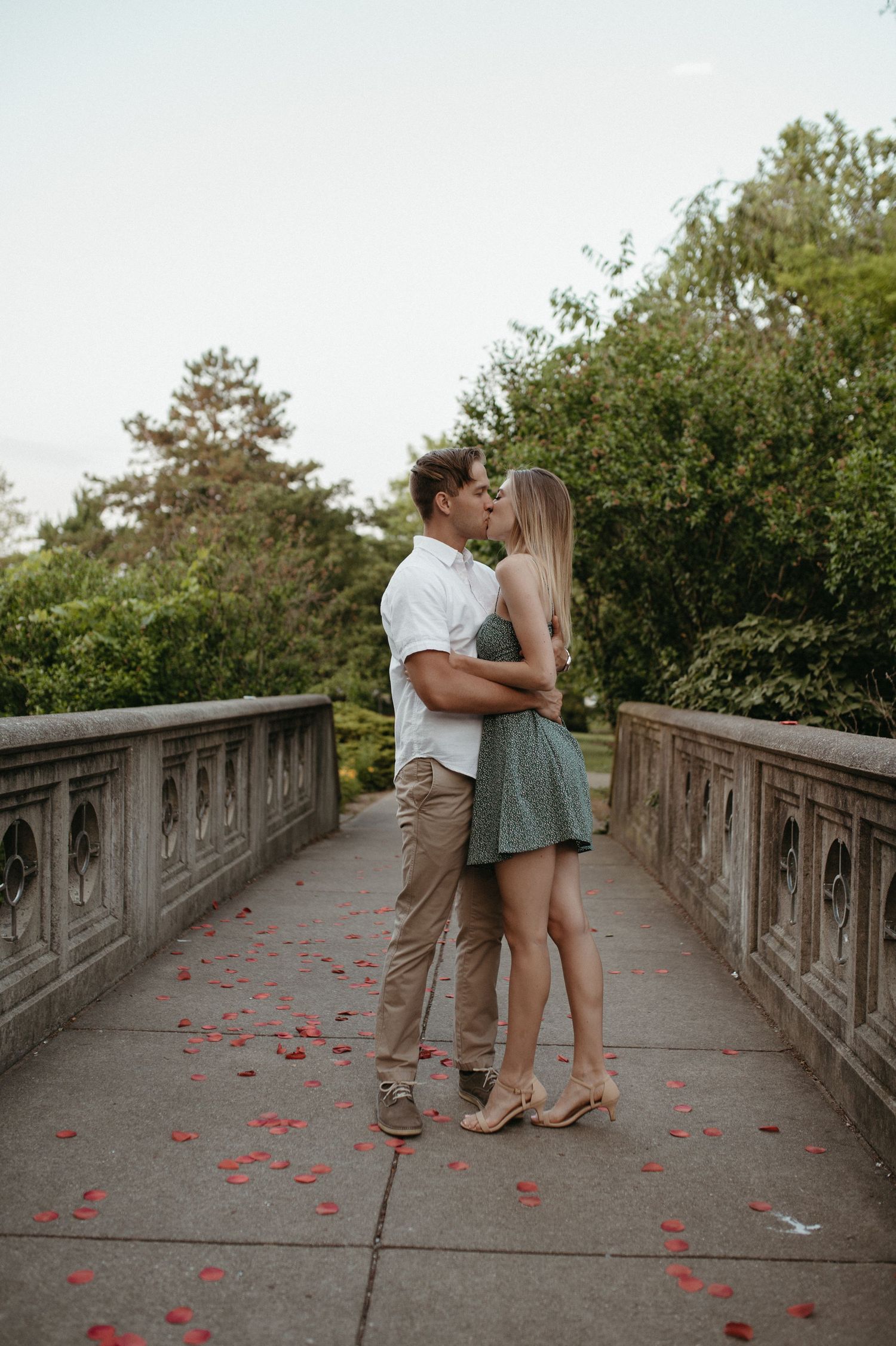 Romantic couple embracing on stone bridge walkway with scattered rose petals.