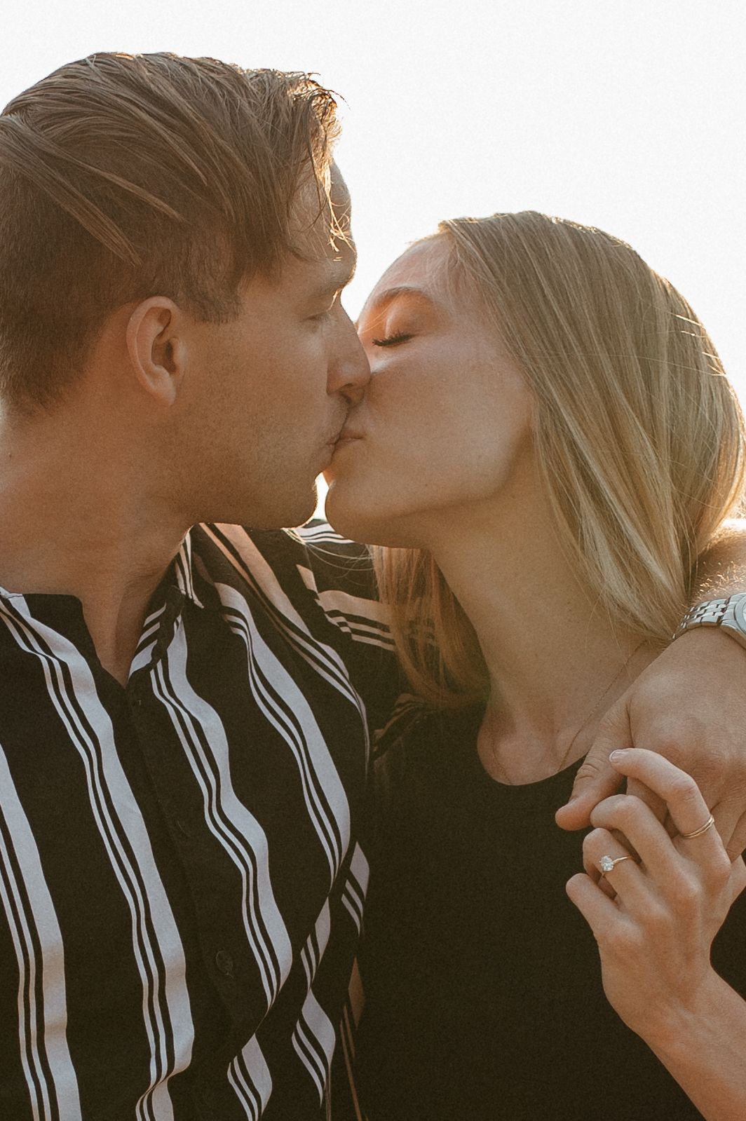 Intimate sunset kiss between couple wearing black and striped clothing.