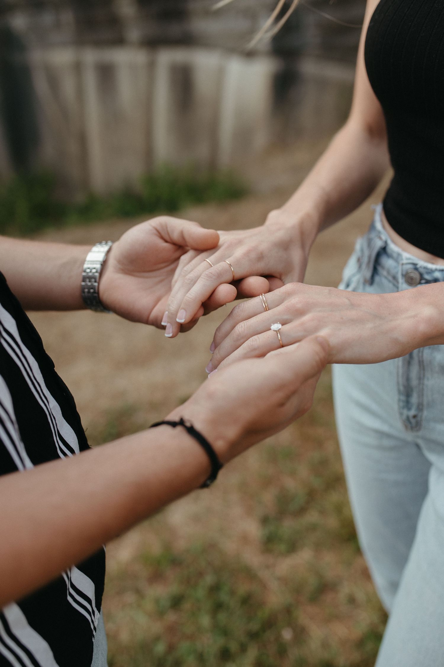 Close-up of hands holding and displaying engagement ring in outdoor setting.