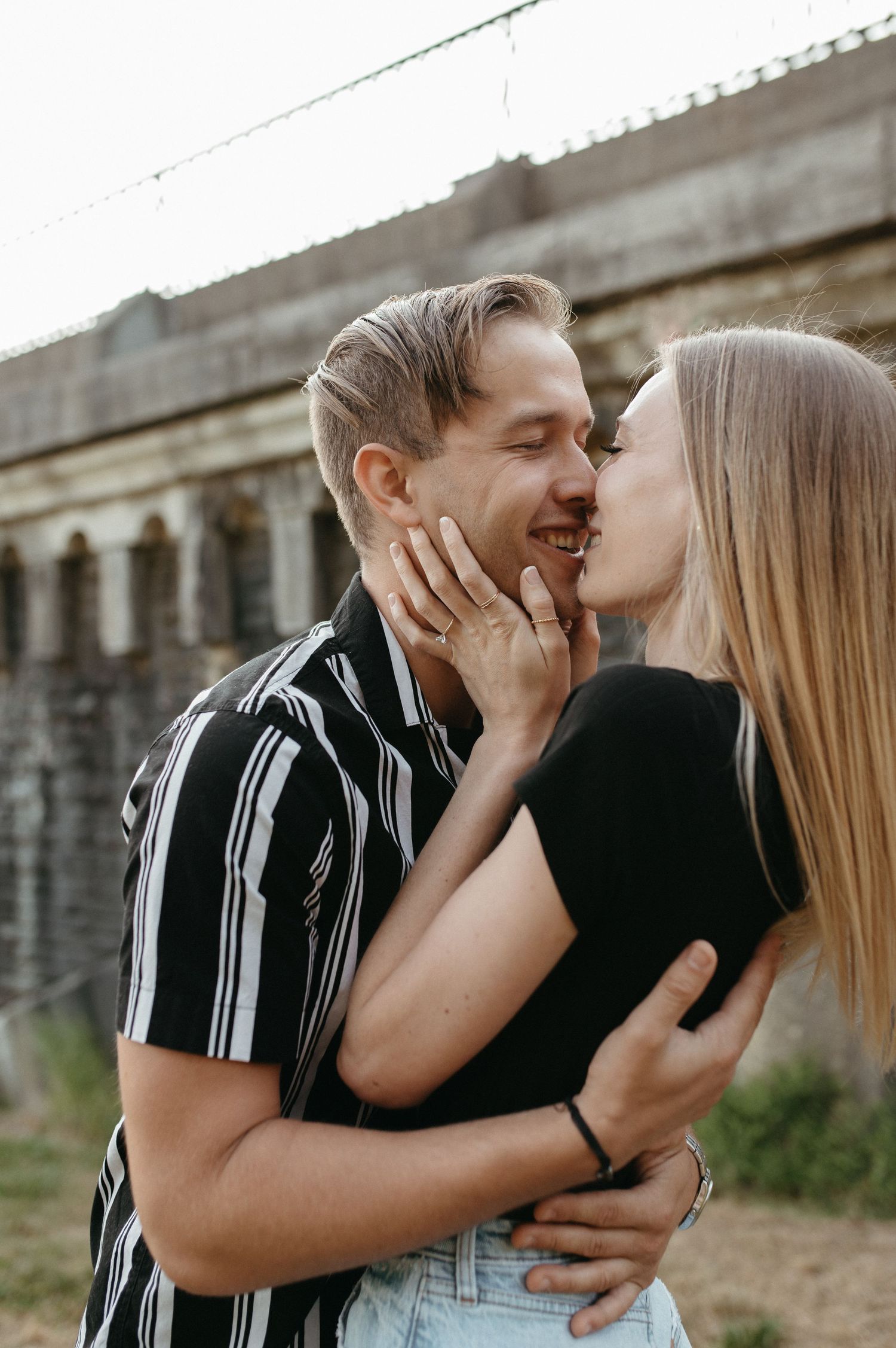 Romantic couple sharing an intimate moment outdoors against a stone wall background.