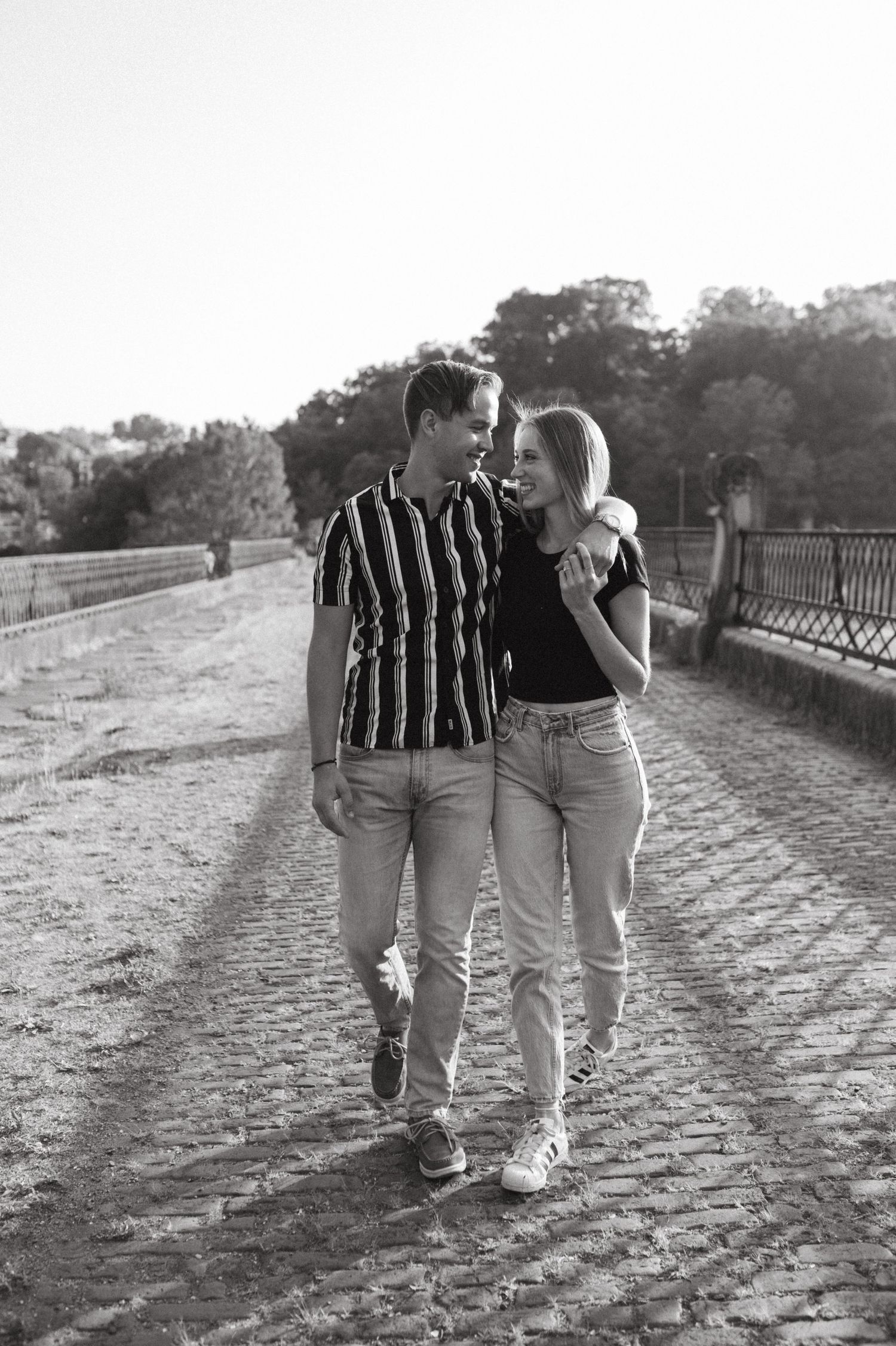 Couple walking and laughing together on a cobblestone path during sunset.