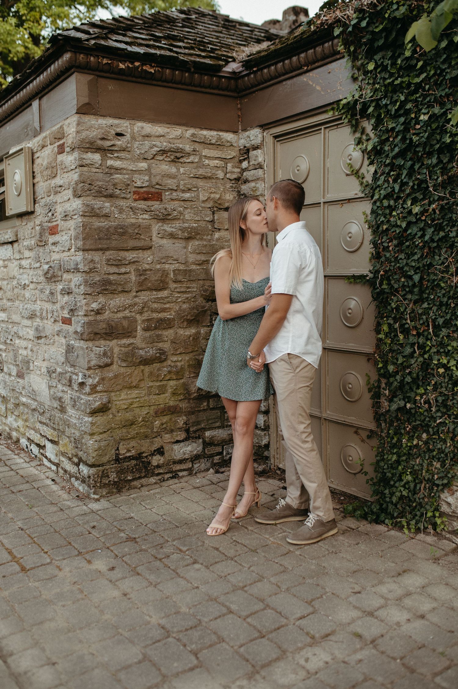 Romantic couple pose against rustic stone wall with decorative door and climbing ivy.