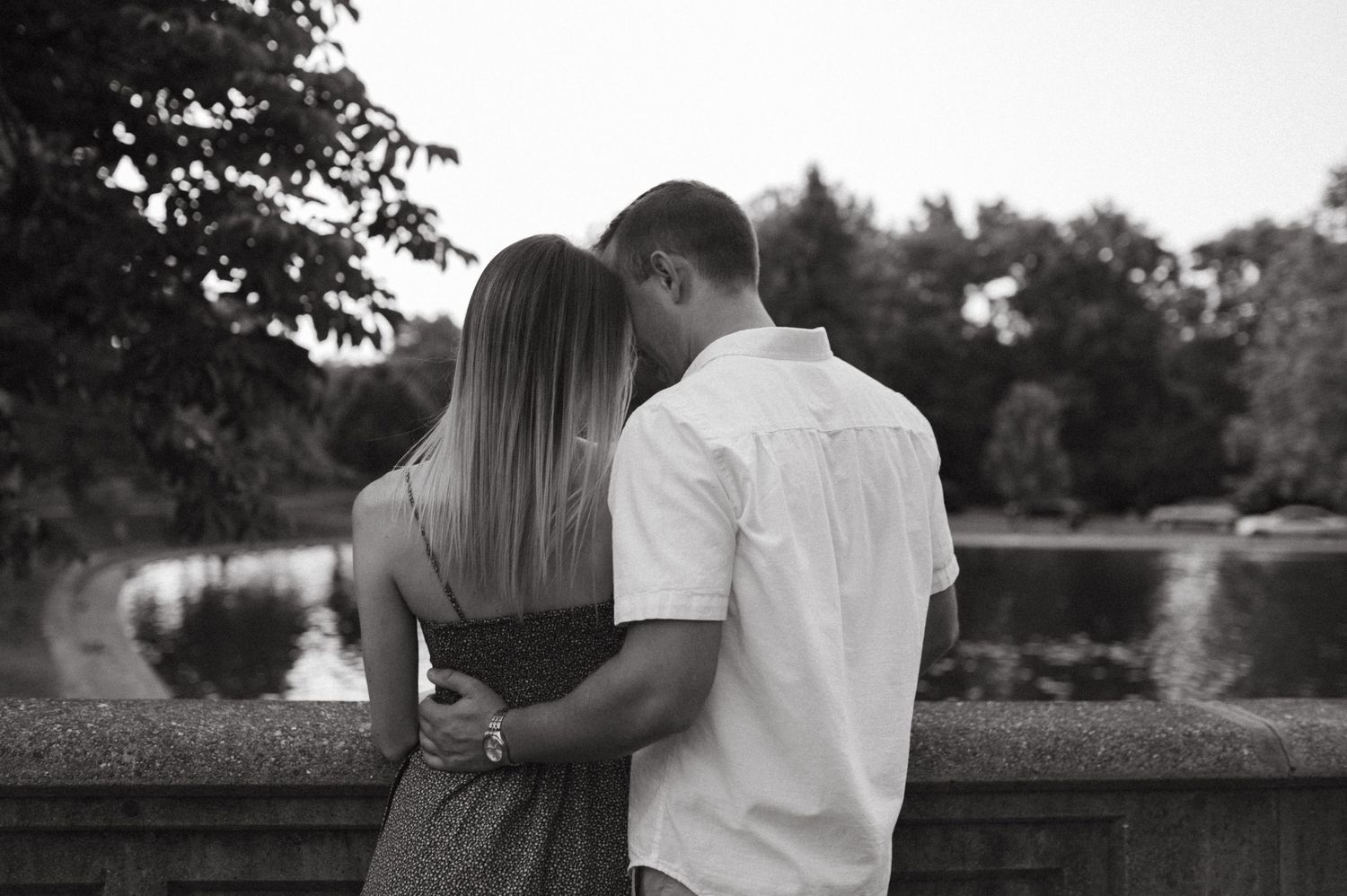 Black and white photo of couple embracing while looking out over scenic overlook.