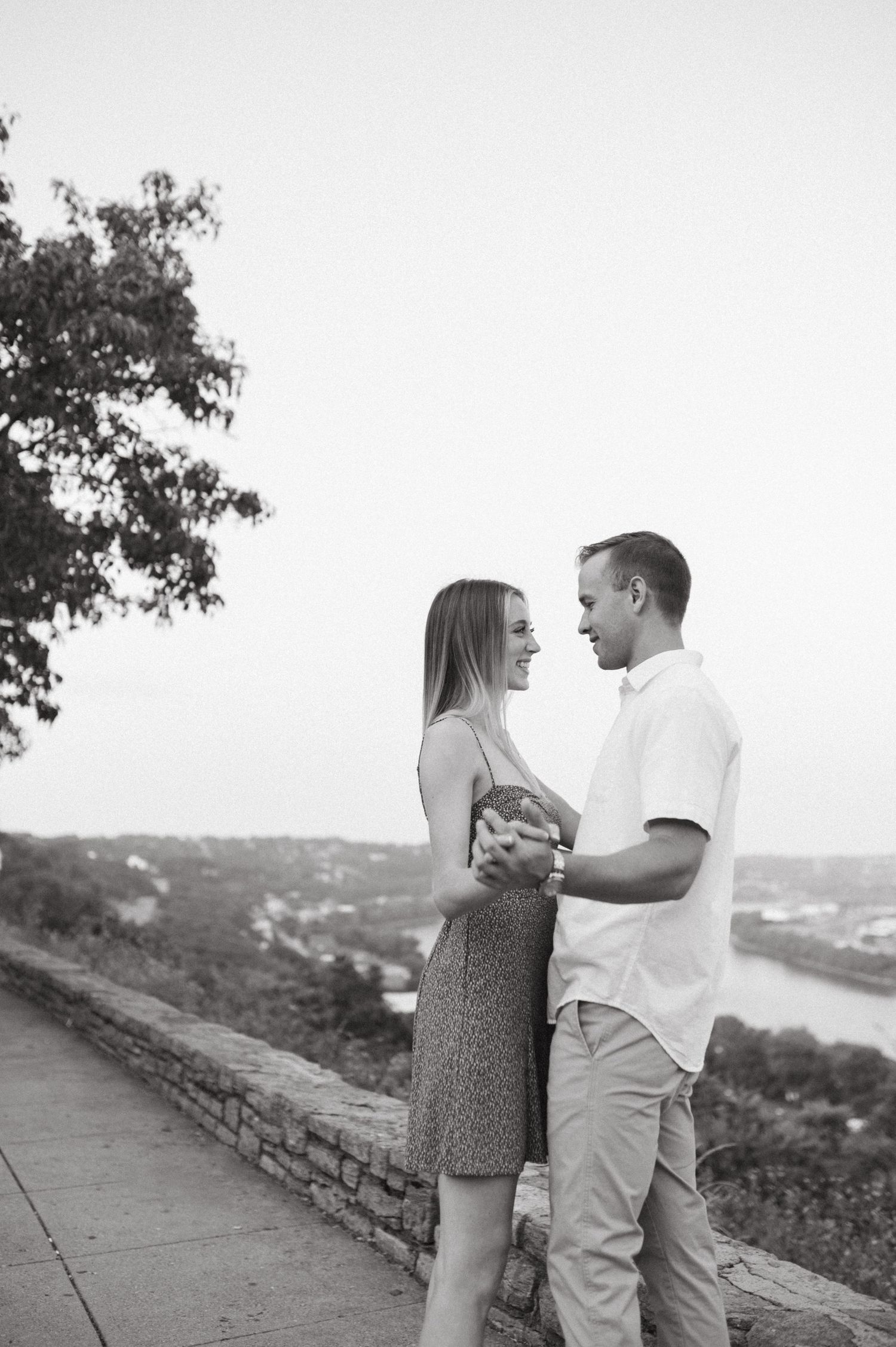 Black and white photo of a couple sharing an intimate moment at a scenic overlook.