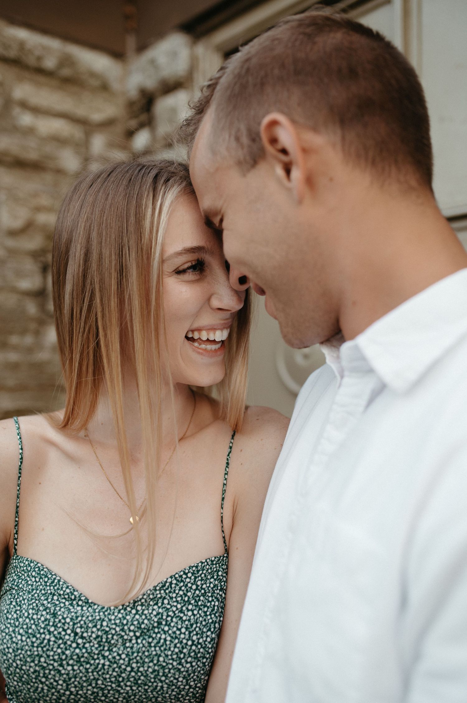 An intimate close-up of a couple sharing a tender moment against a stone wall backdrop.