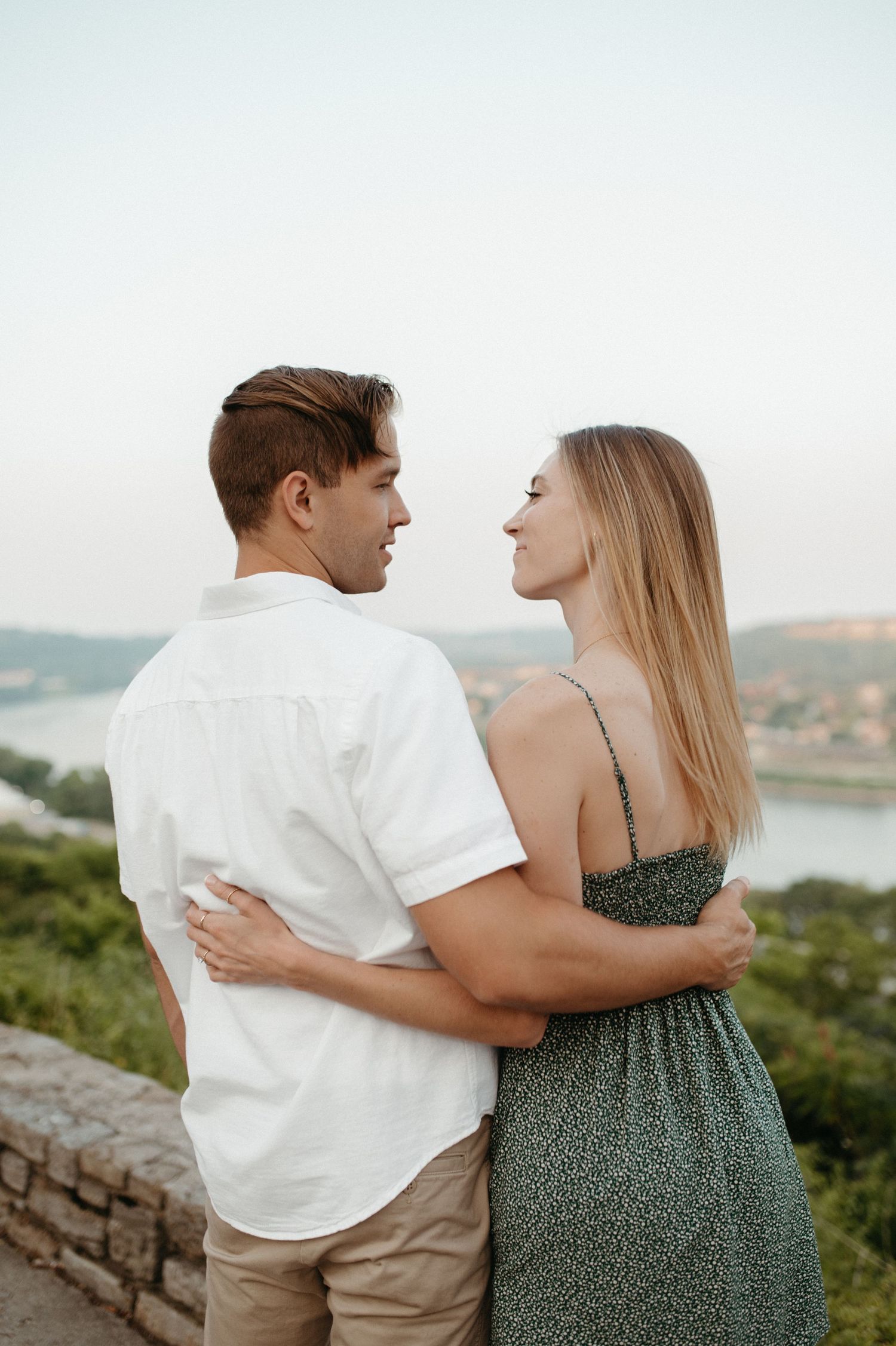 A romantic couple embraces while enjoying a scenic overlook of a river valley on a summer evening.