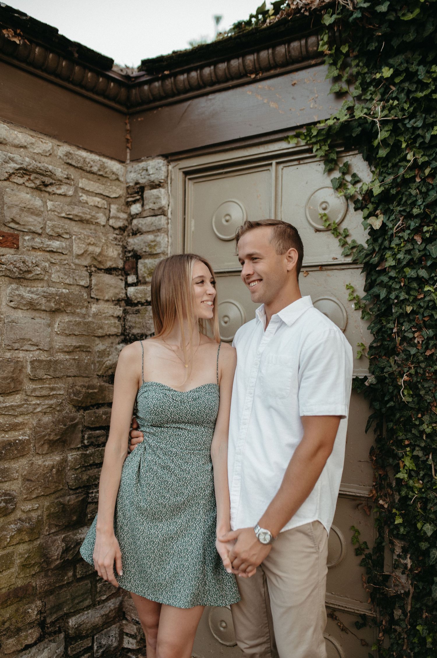 Couple in summer attire posing together against a stone wall with vintage door and climbing vines.