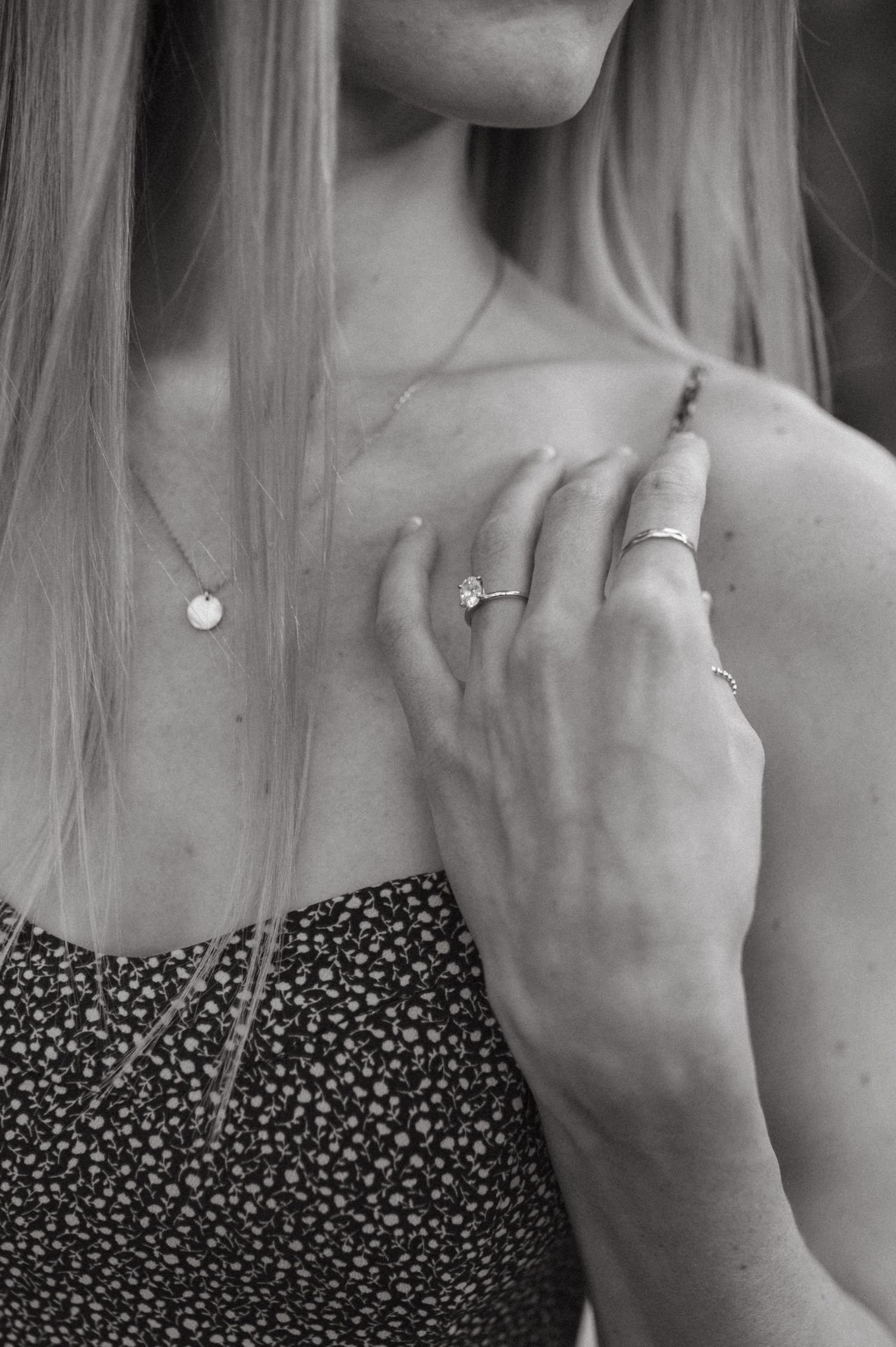 Close-up shot of a hand wearing delicate jewelry including rings and a necklace against a floral dress.
