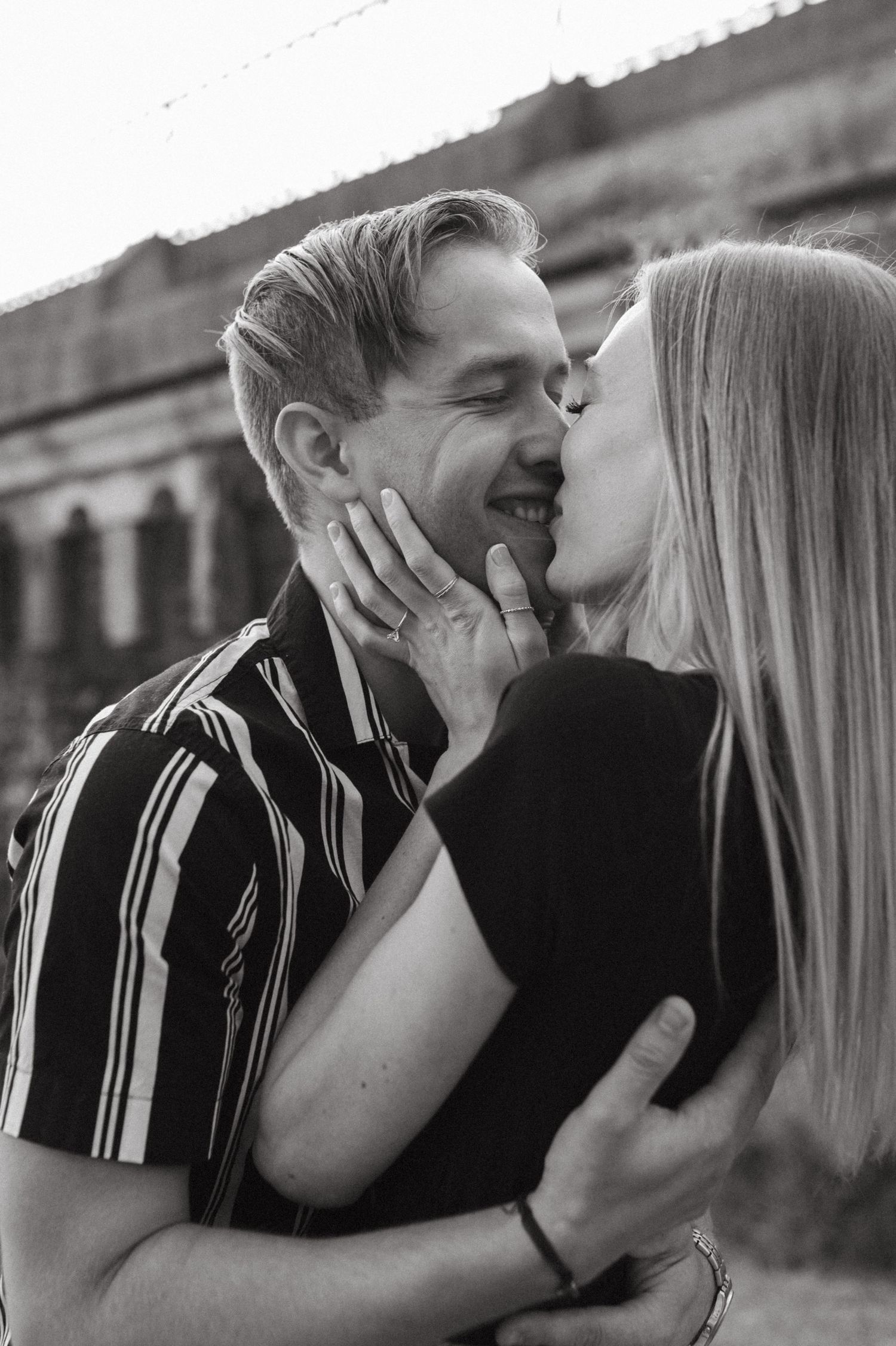 Black and white portrait of a tender moment between a couple against architectural backdrop.