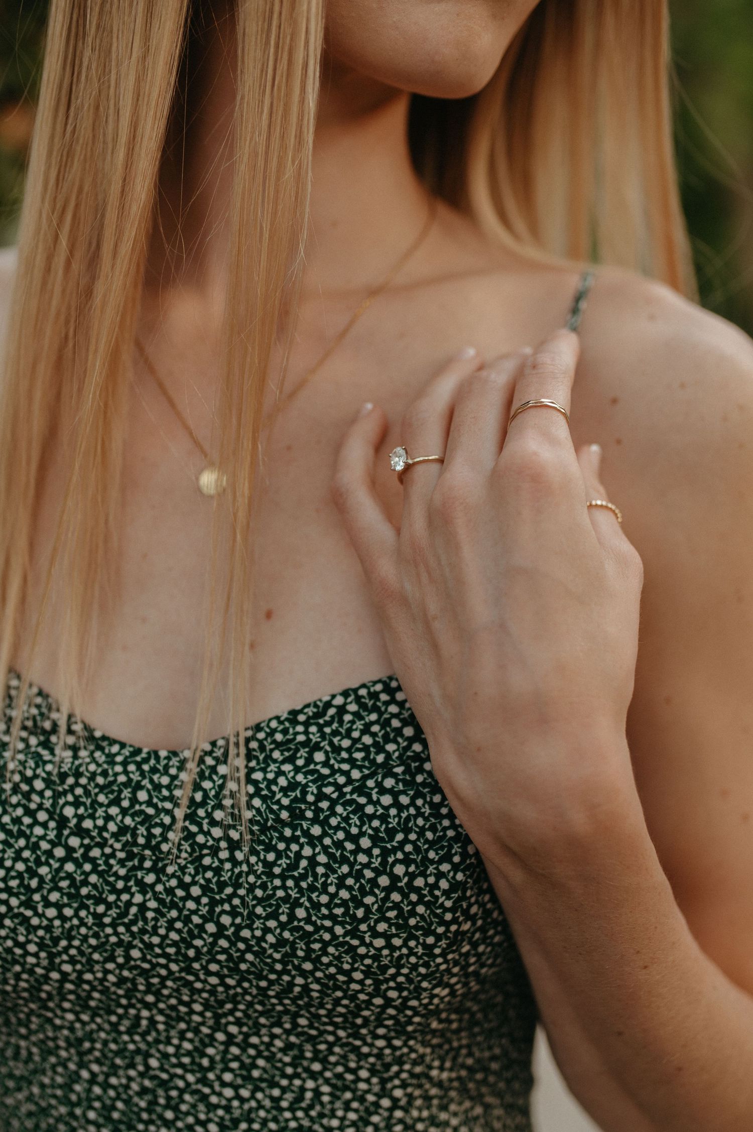 Detail shot of engagement ring and jewelry worn with a green floral patterned dress.