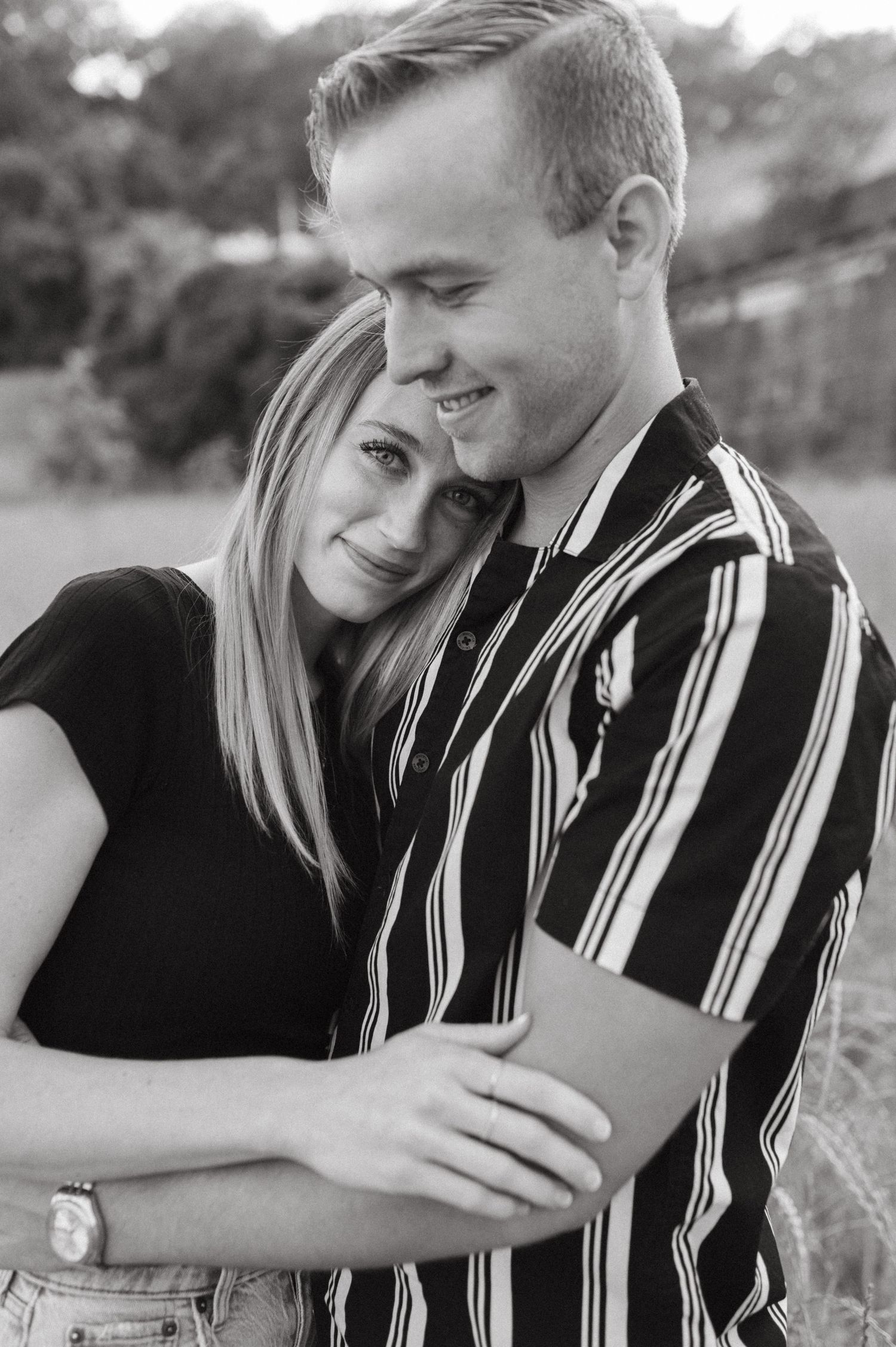 Black and white portrait of couple in casual attire sharing affectionate moment outdoors.