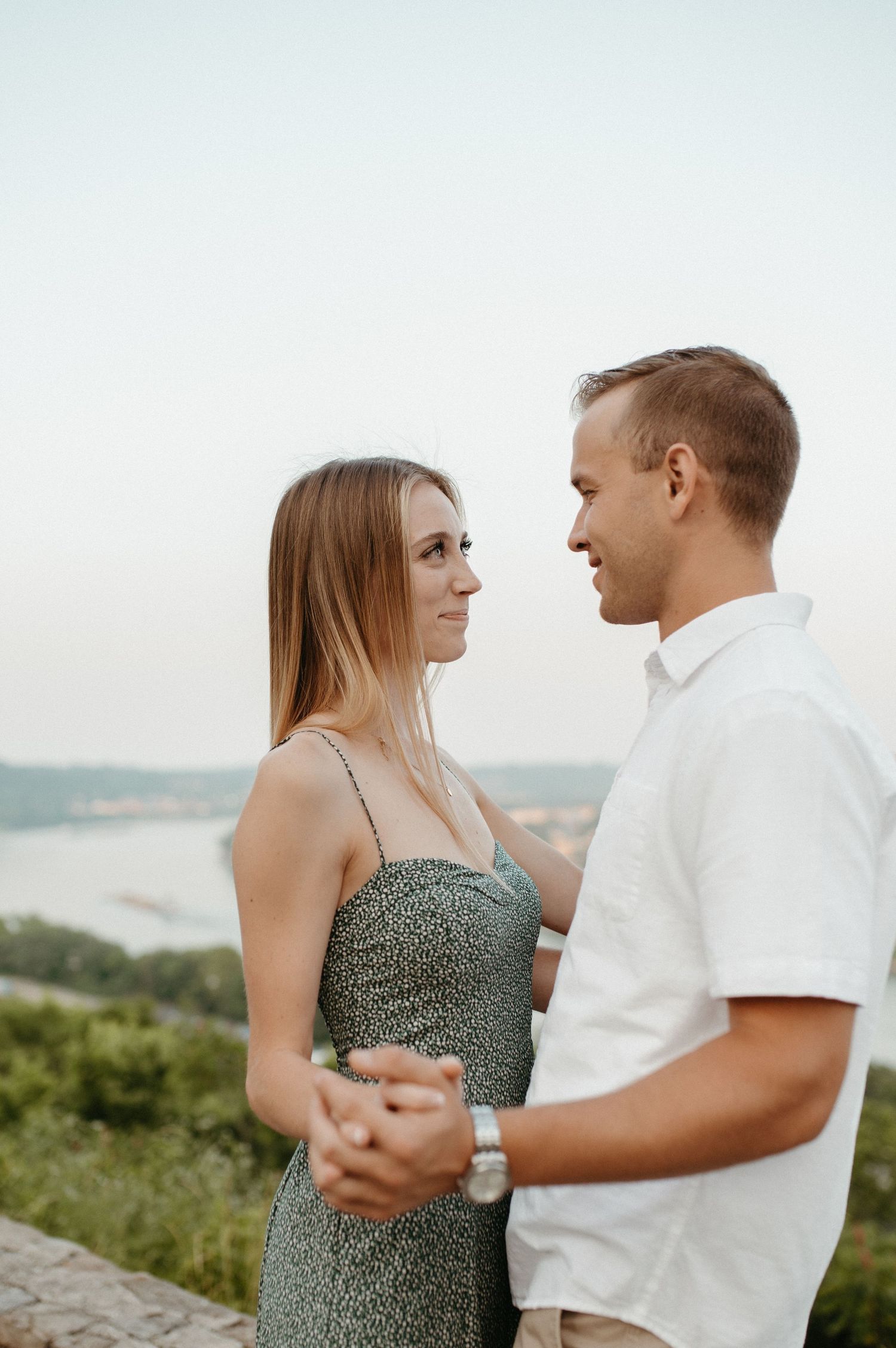 Couple in summer attire dancing together on an outdoor overlook with river views.