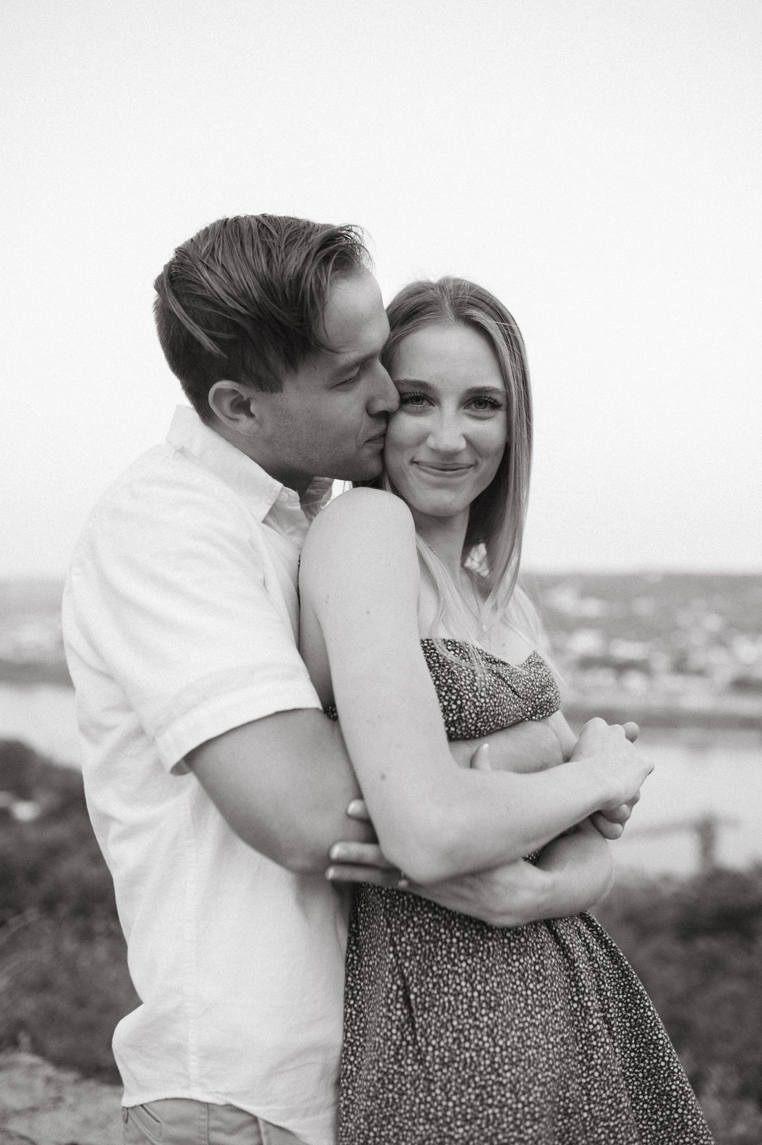 Black and white portrait of couple sharing tender moment at scenic overlook.