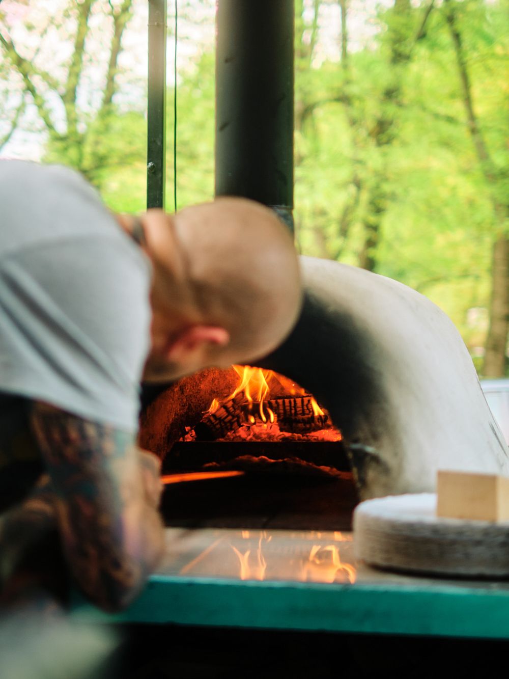 Chef checking pizza cooking in a wood-fired outdoor oven.