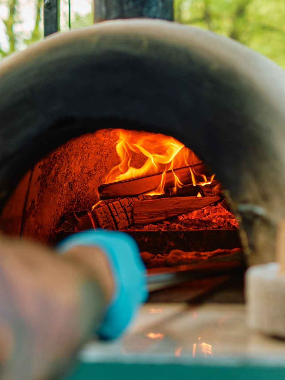 Wood-fired pizza oven with bright flames visible through the dome opening.