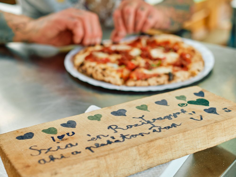 Pizza being served with decorative wooden board featuring heart designs.