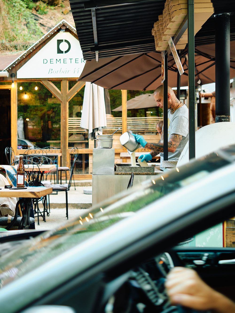 Outdoor restaurant seating area with wooden pergola and Demeter signage.