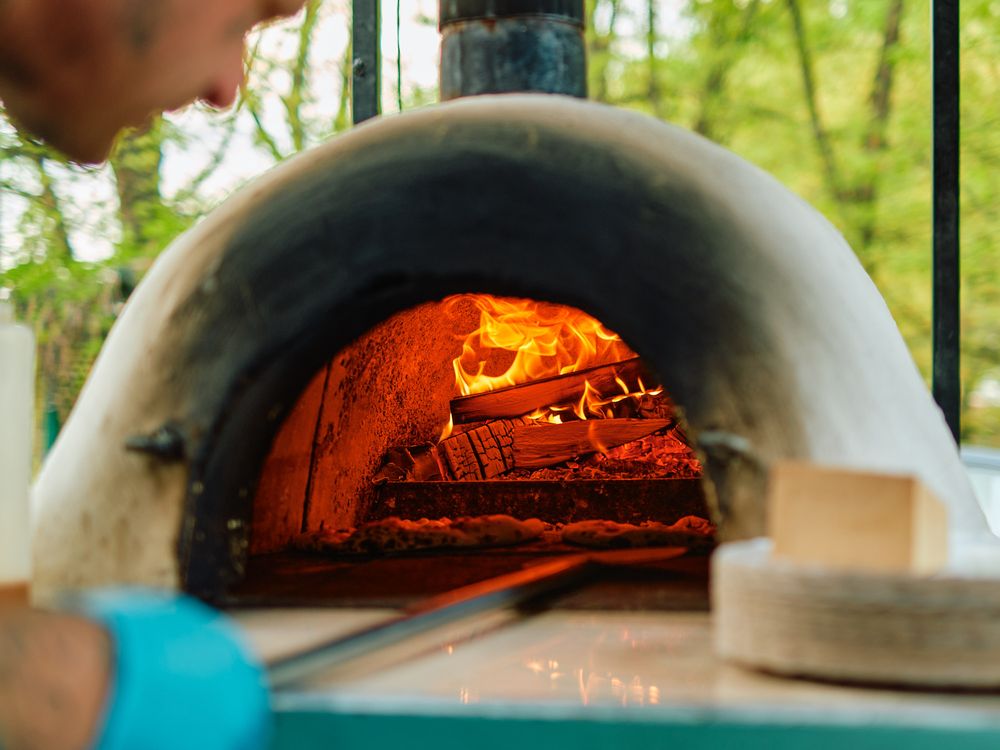 Close-up view of a traditional brick pizza oven with burning wood and flames inside.