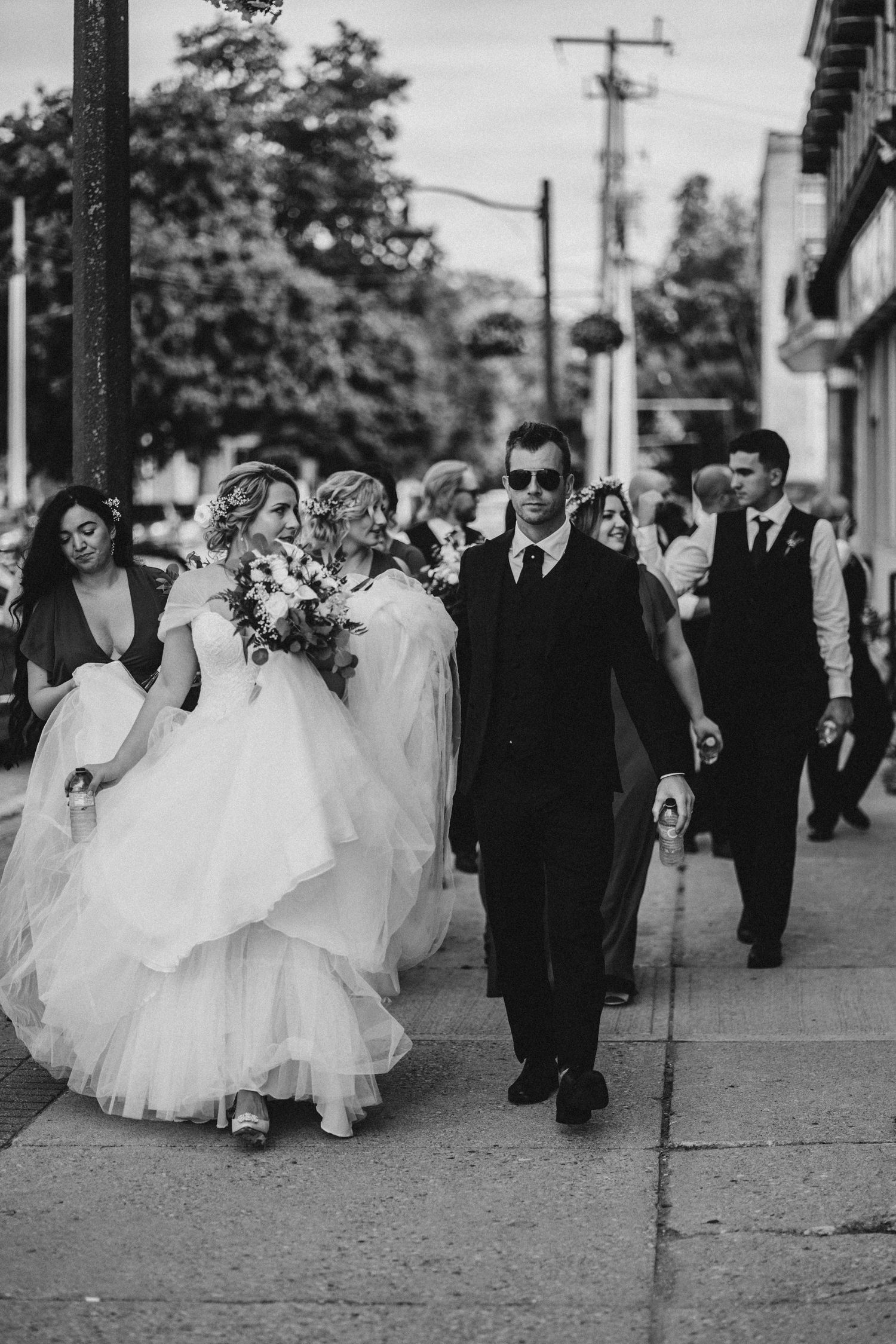 Image of bride and groom walking down street with bridal party.