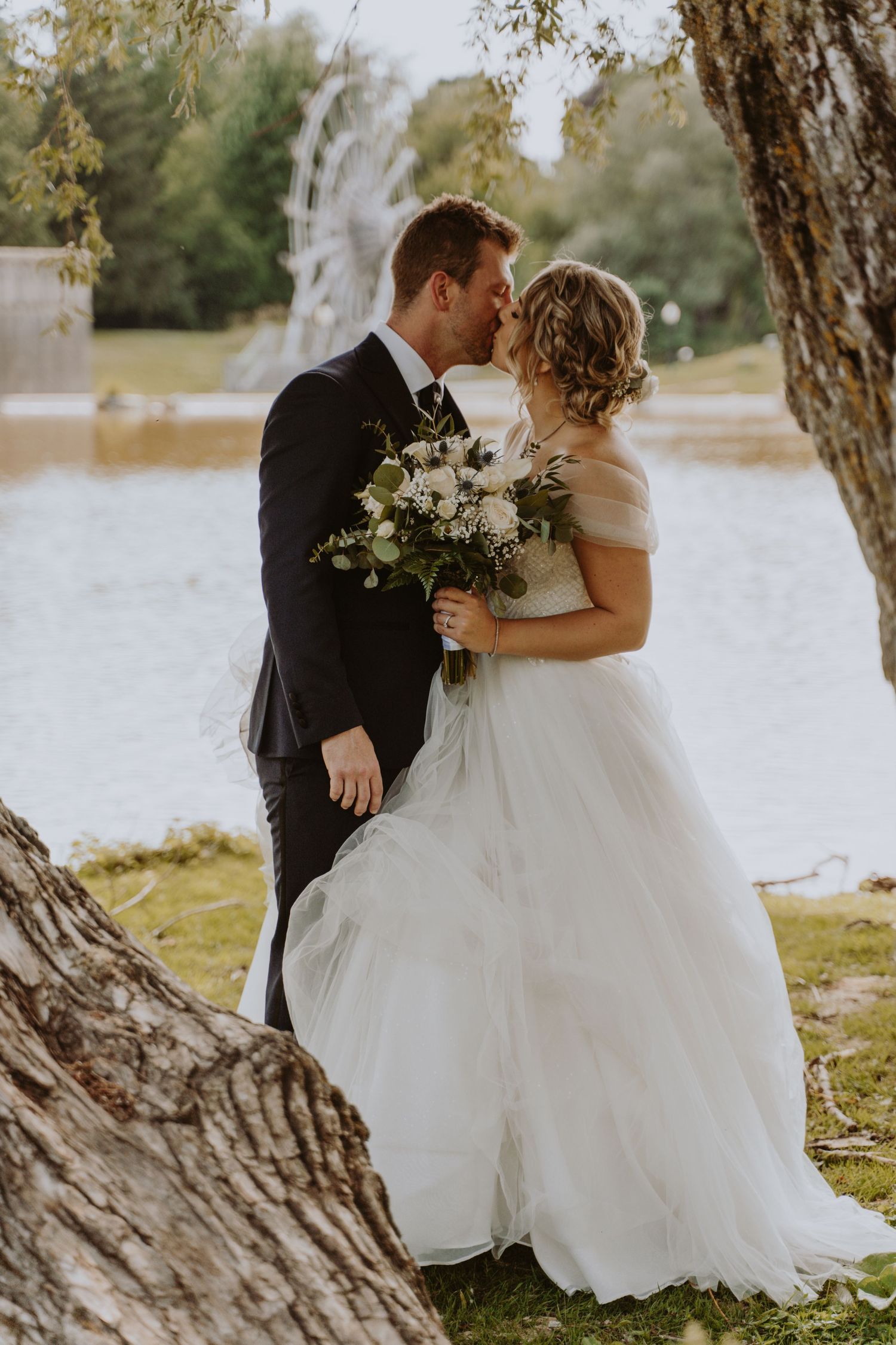 Image of bride and groom kissing under tree.