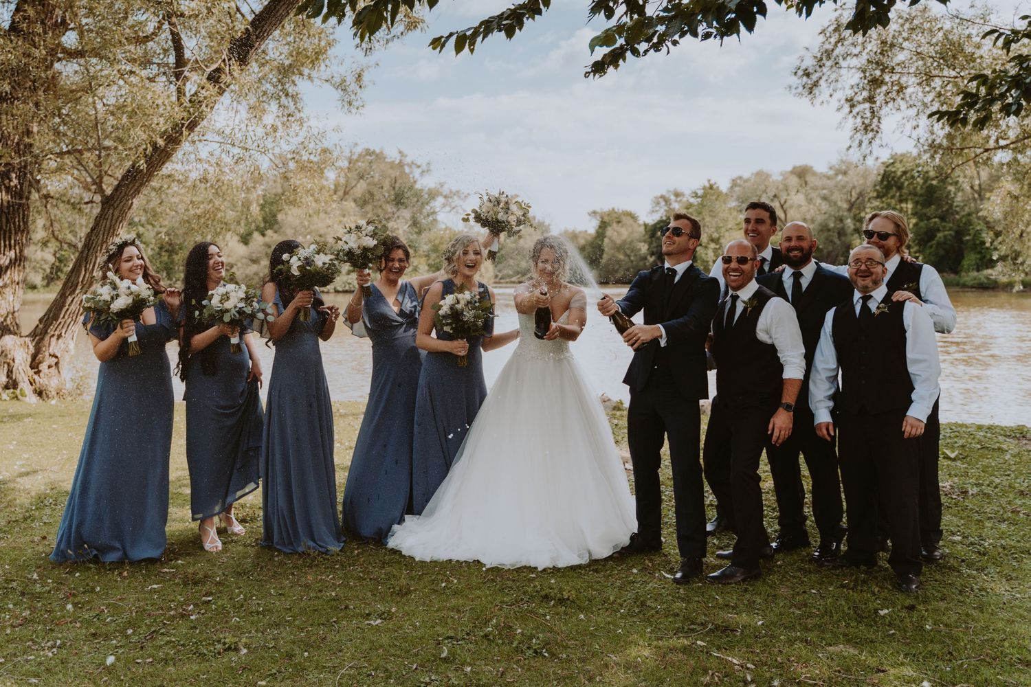 Image of bridal party in front of water popping champagne.