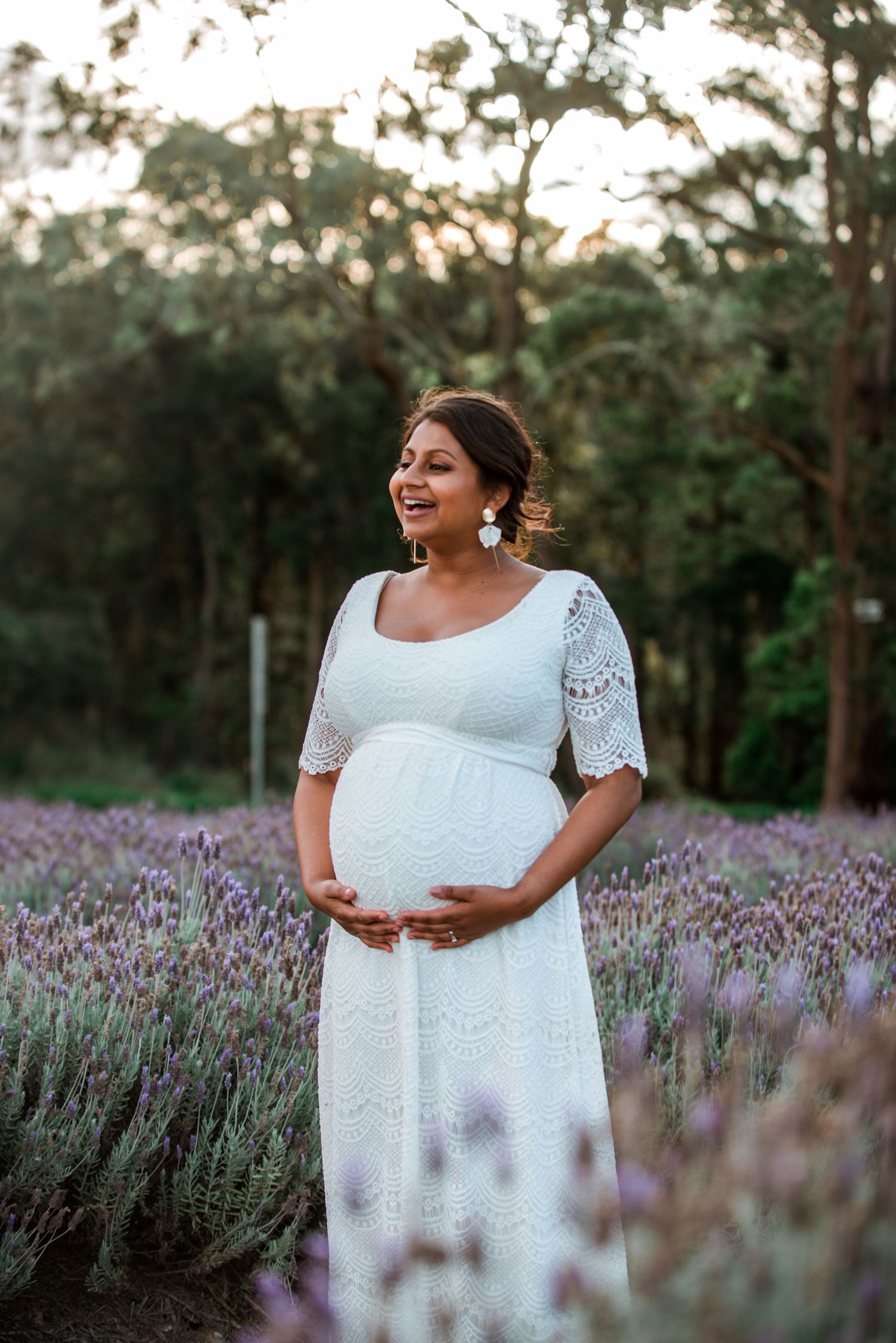 A person in a white lace dress stands joyfully in a blooming lavender field during sunset.