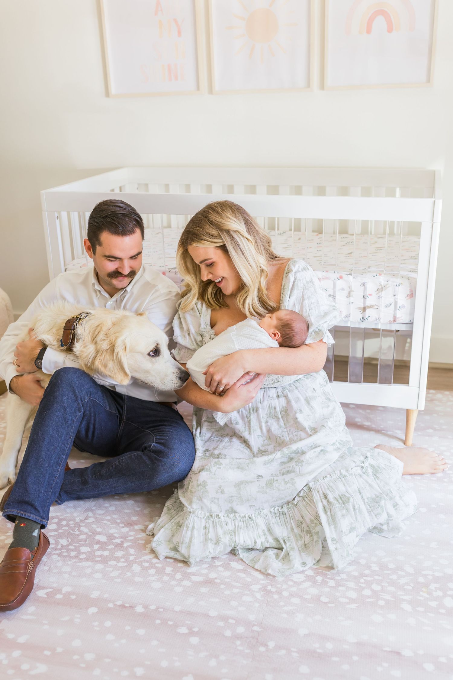 Candid family moment with dog and newborn baby relaxing by white crib.
