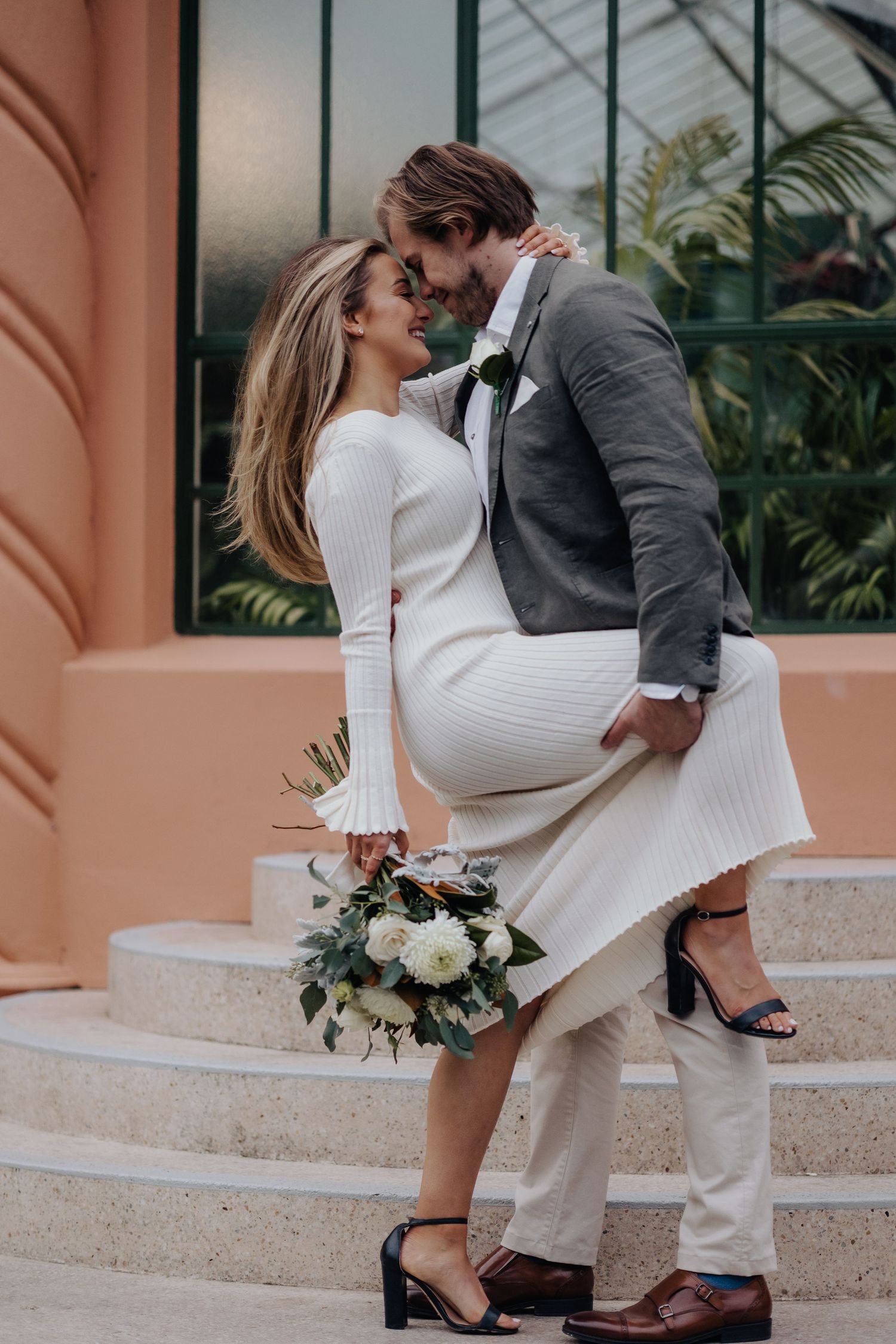 Romantic pose on salmon-colored steps with bride holding white floral bouquet.