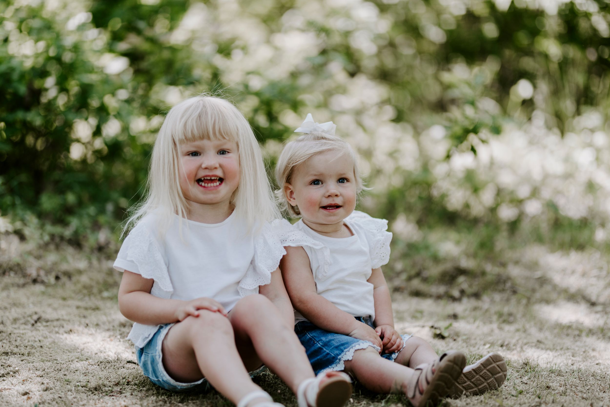 Two young children sit together on the ground laughing and playing outdoors.