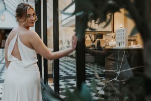a model walking in an alleyway  leaning on a window wearing a white wedding dress in silk in Brighton