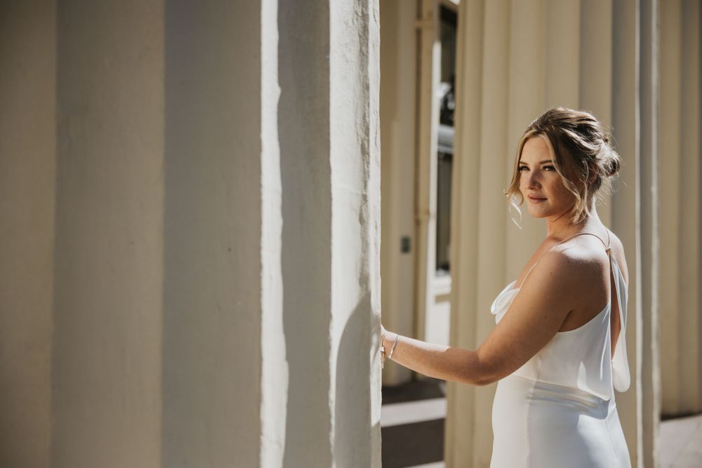 a model wearing a silk wedding dress leaning against a pillar outside Brighton Town hall