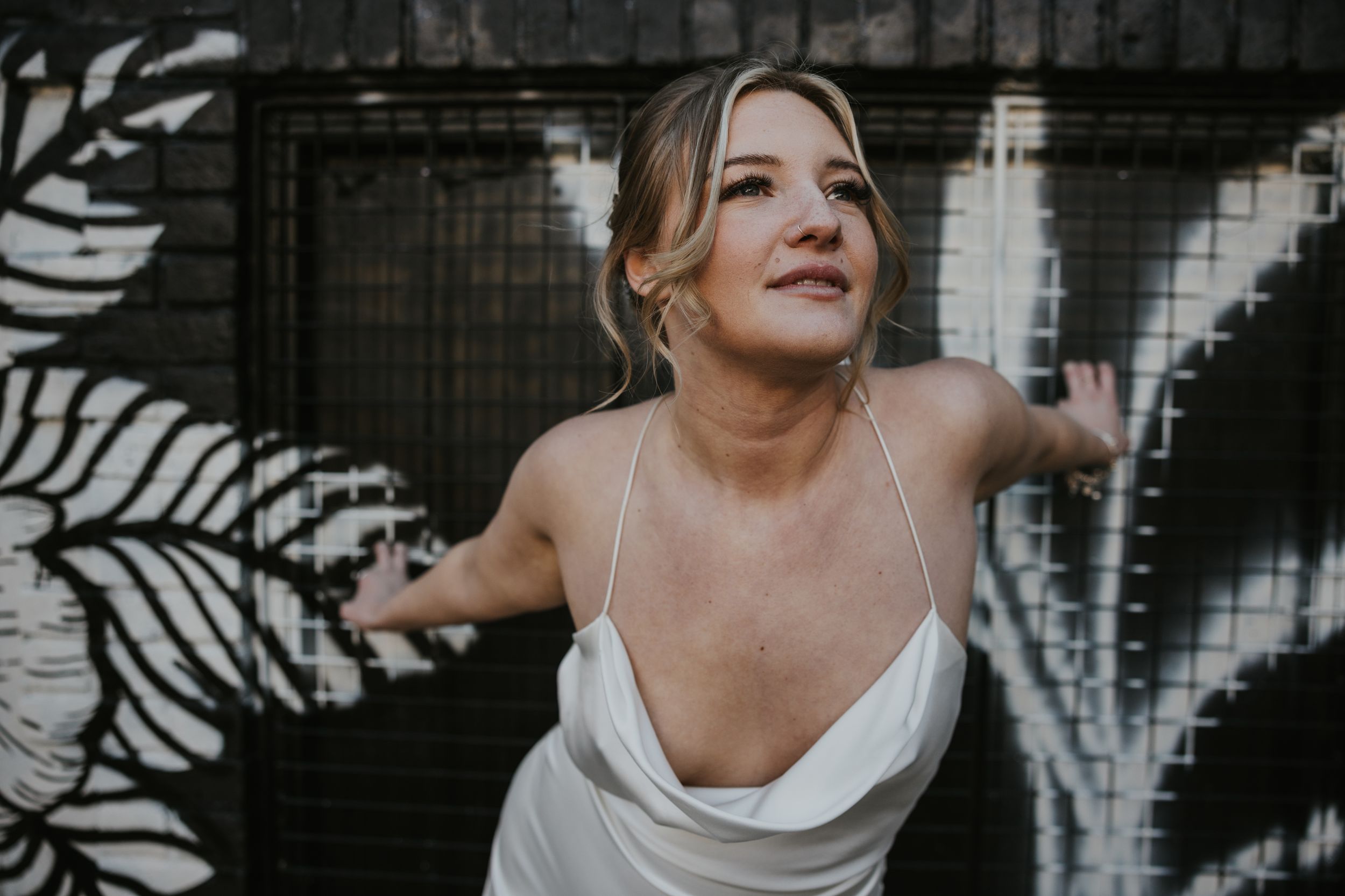 a white blonde model in a white wedding dress standing by a wall of black and white graffiti in Brighton