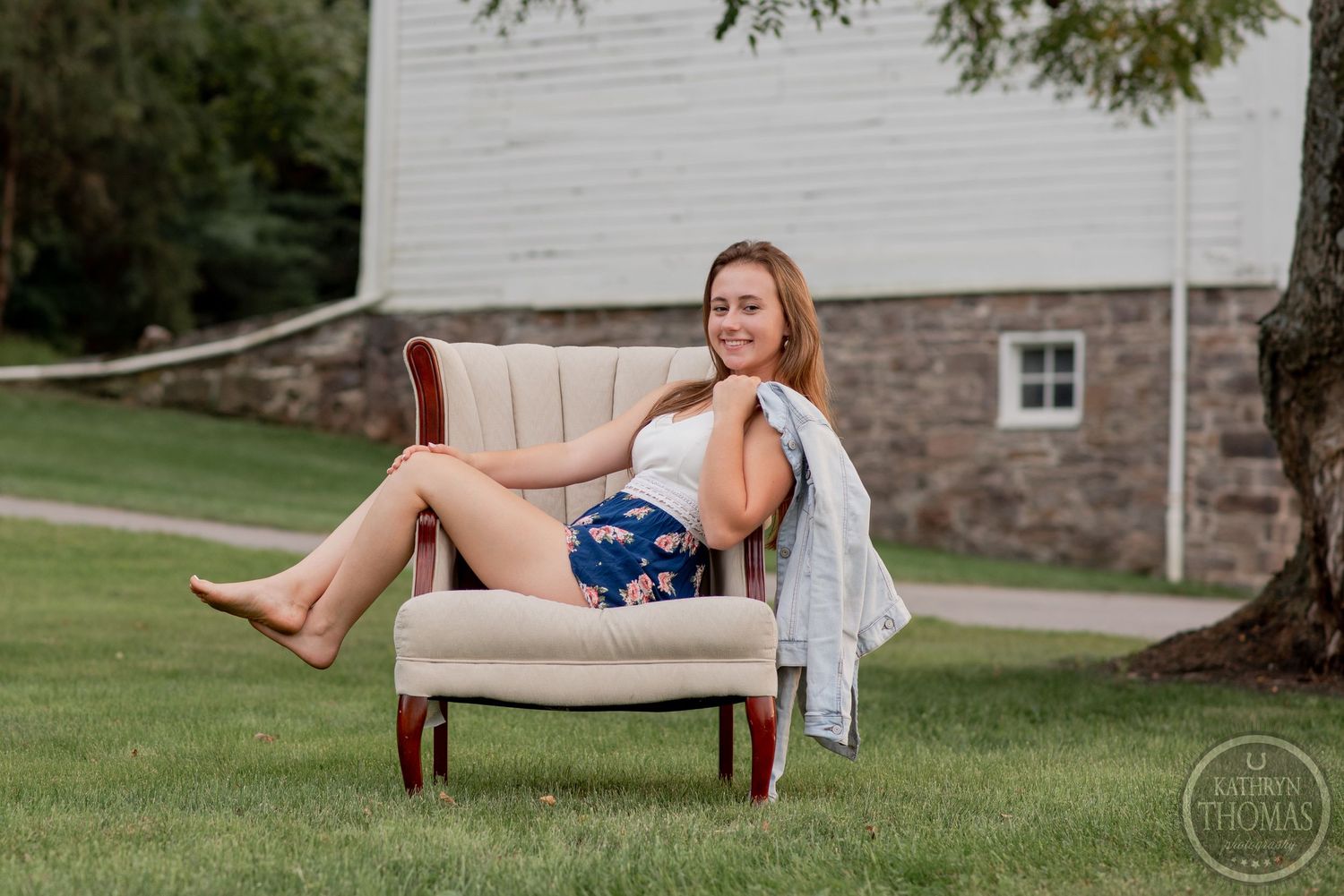 Relaxed portrait of someone lounging on beige armchair outdoors wearing casual summer attire.