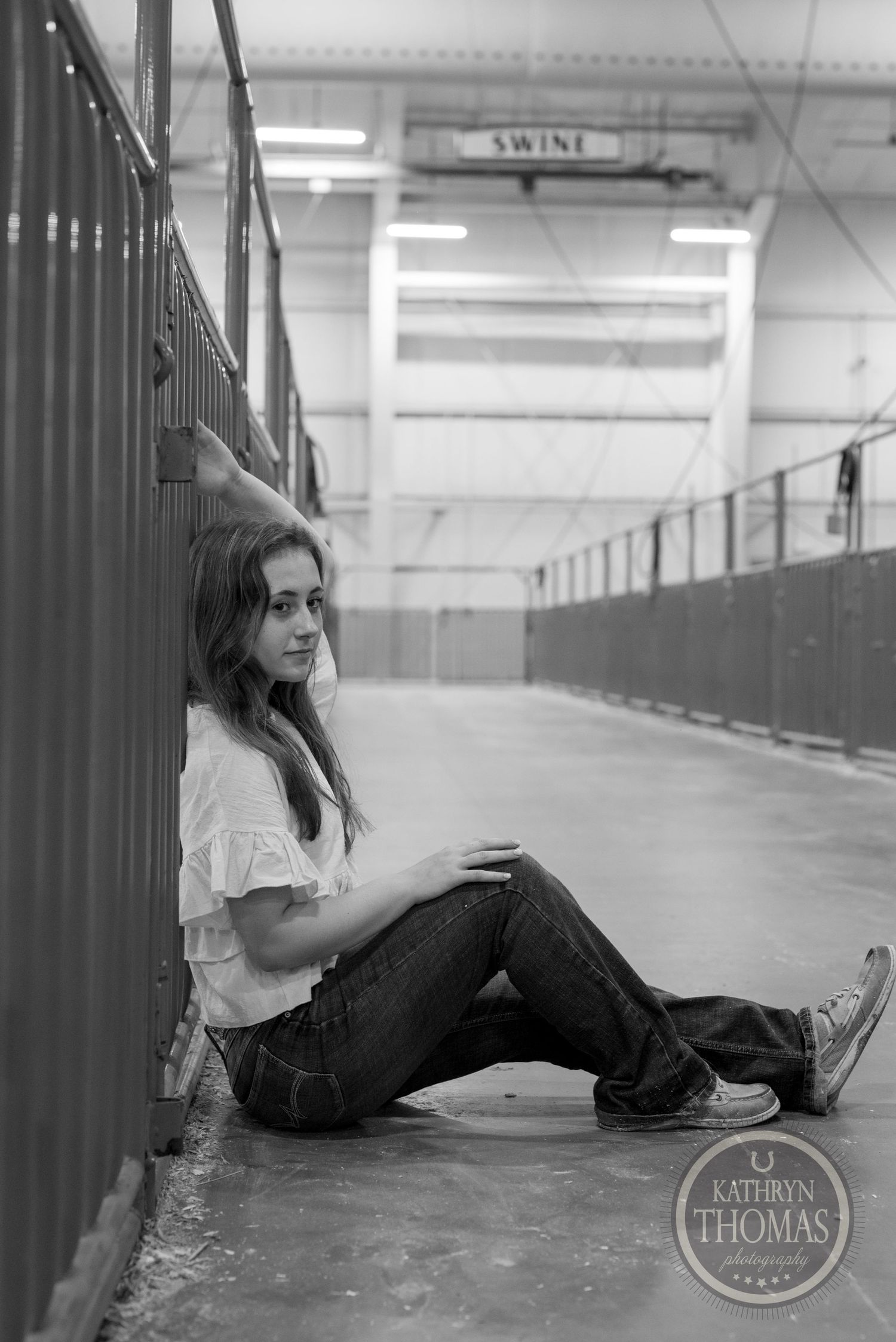 A black and white photo of someone sitting against a hallway railing in casual attire.