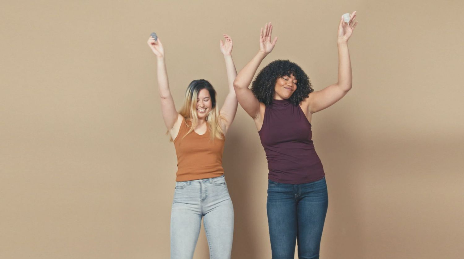 Two friends celebrating with raised arms against neutral background.