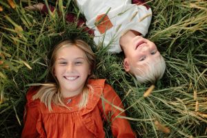 Children lying in tall grass wearing orange clothing while laughing and playing.