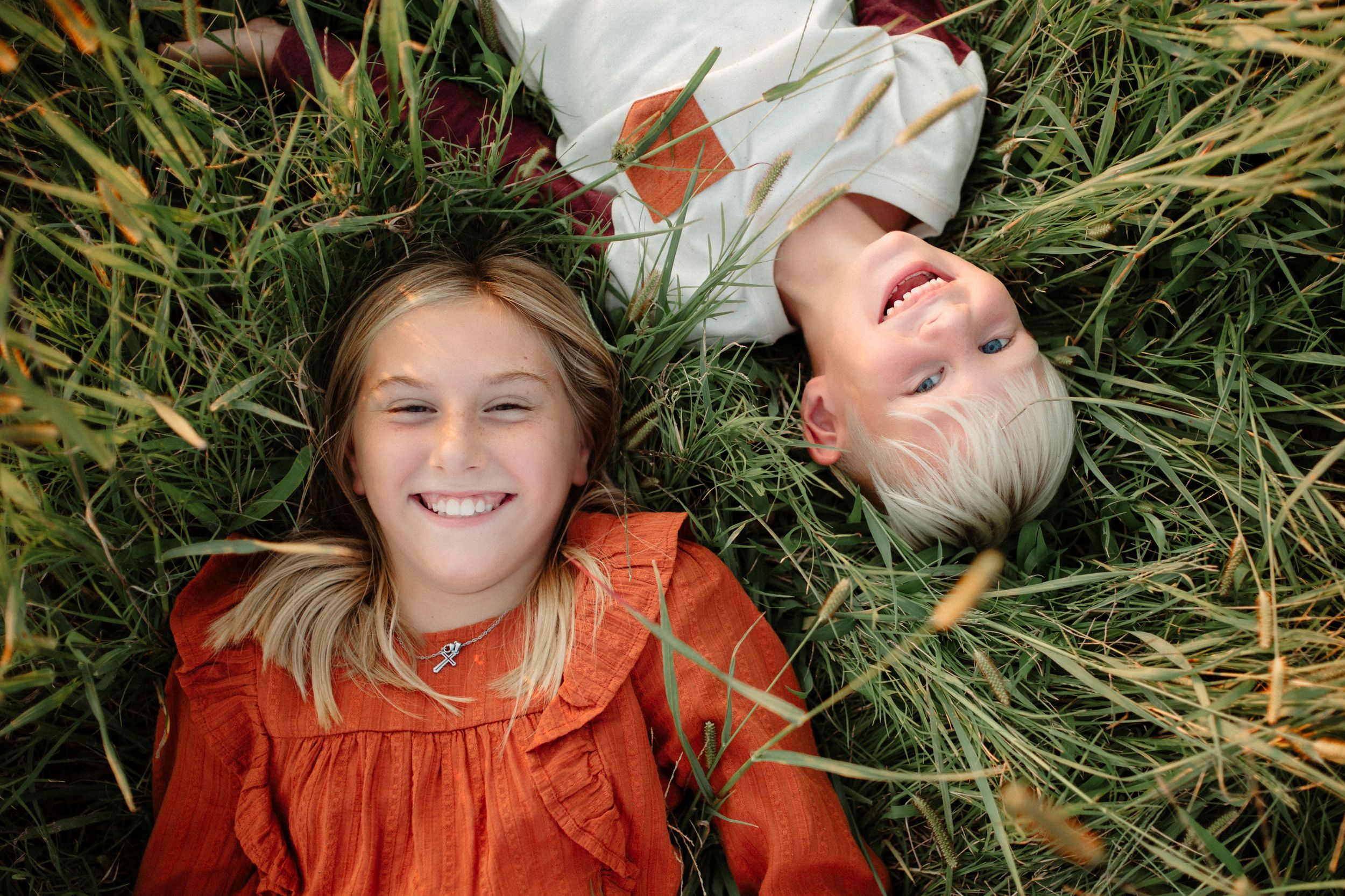 Children lying in tall grass wearing orange clothing while laughing and playing.