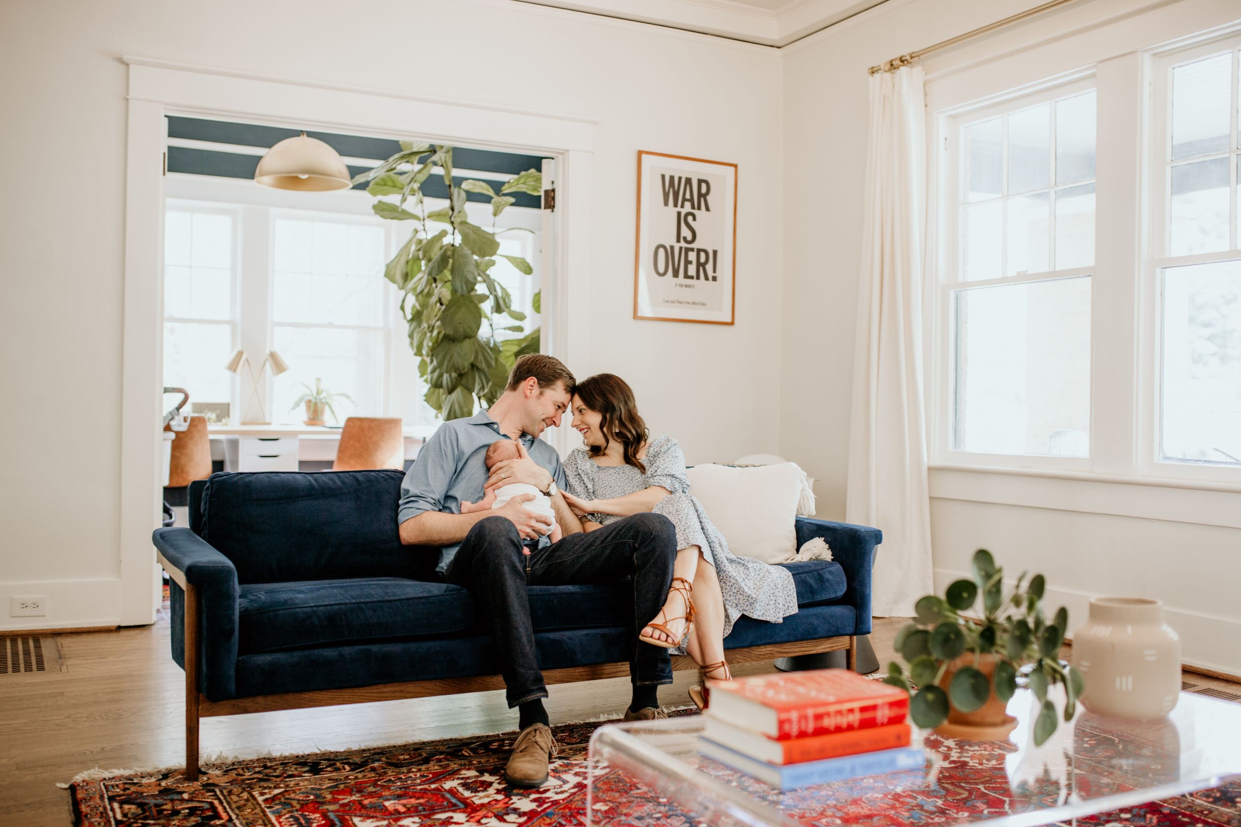 A couple relaxes together on a navy blue couch in a bright, modern living room with white walls and indoor plants.