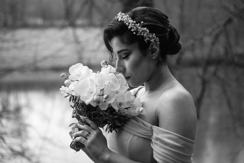 Black and white portrait of a bride in an off-shoulder gown holding a bouquet of white peonies.