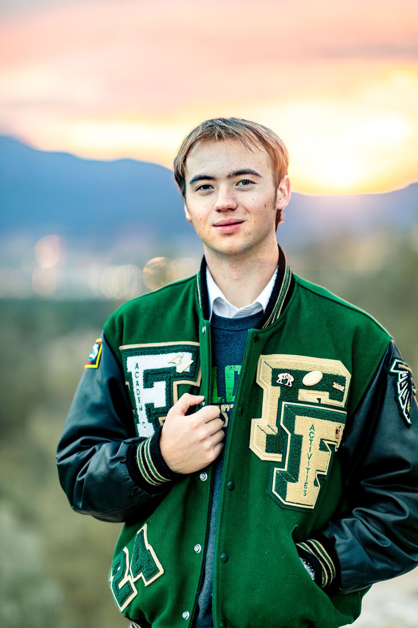 Senior guy smiles posing in letter jacket at his senior session at Palmer Park in Colorado Springs.
