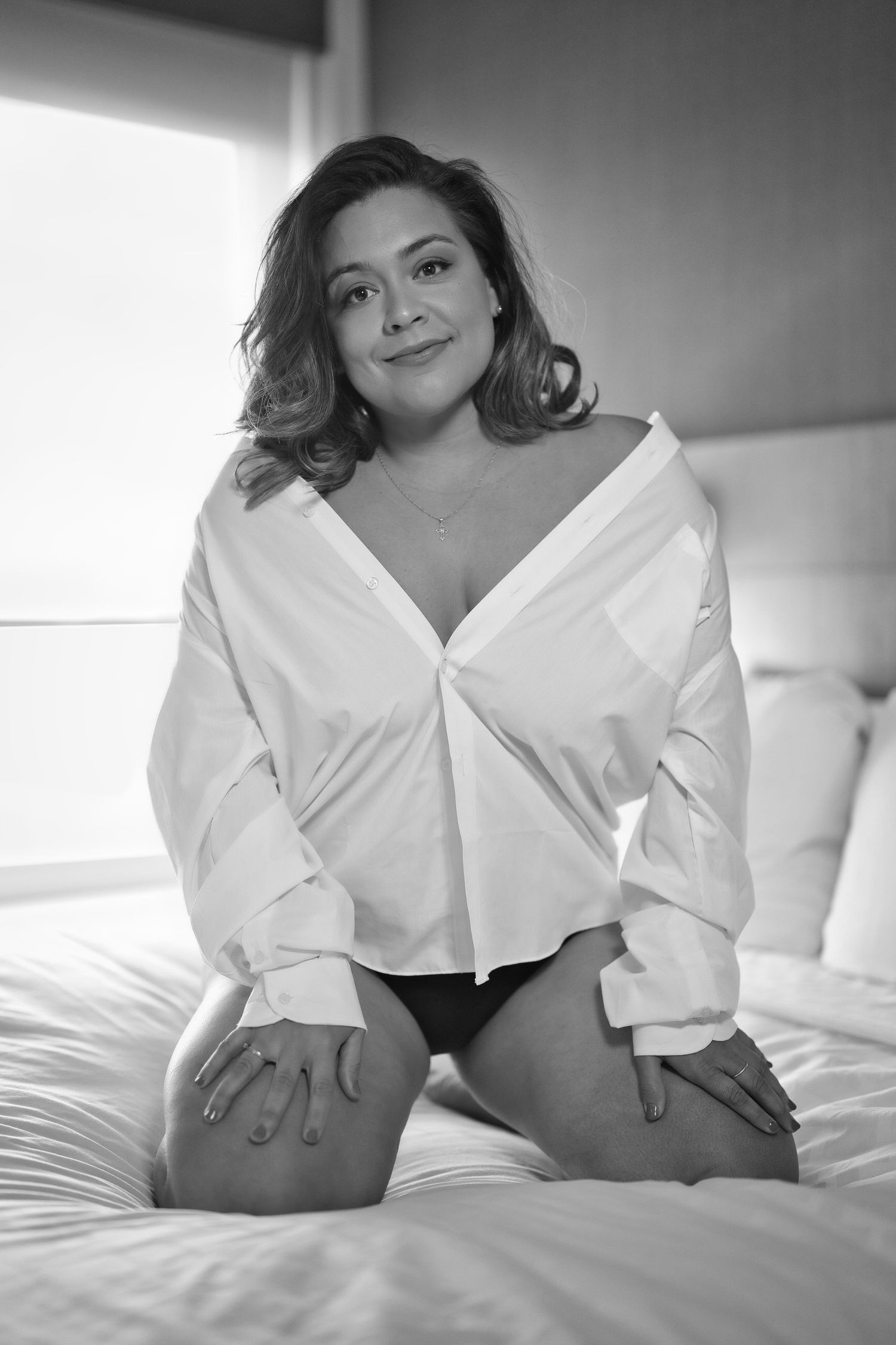 Black and white portrait of a person in white shirt posing on a bed.