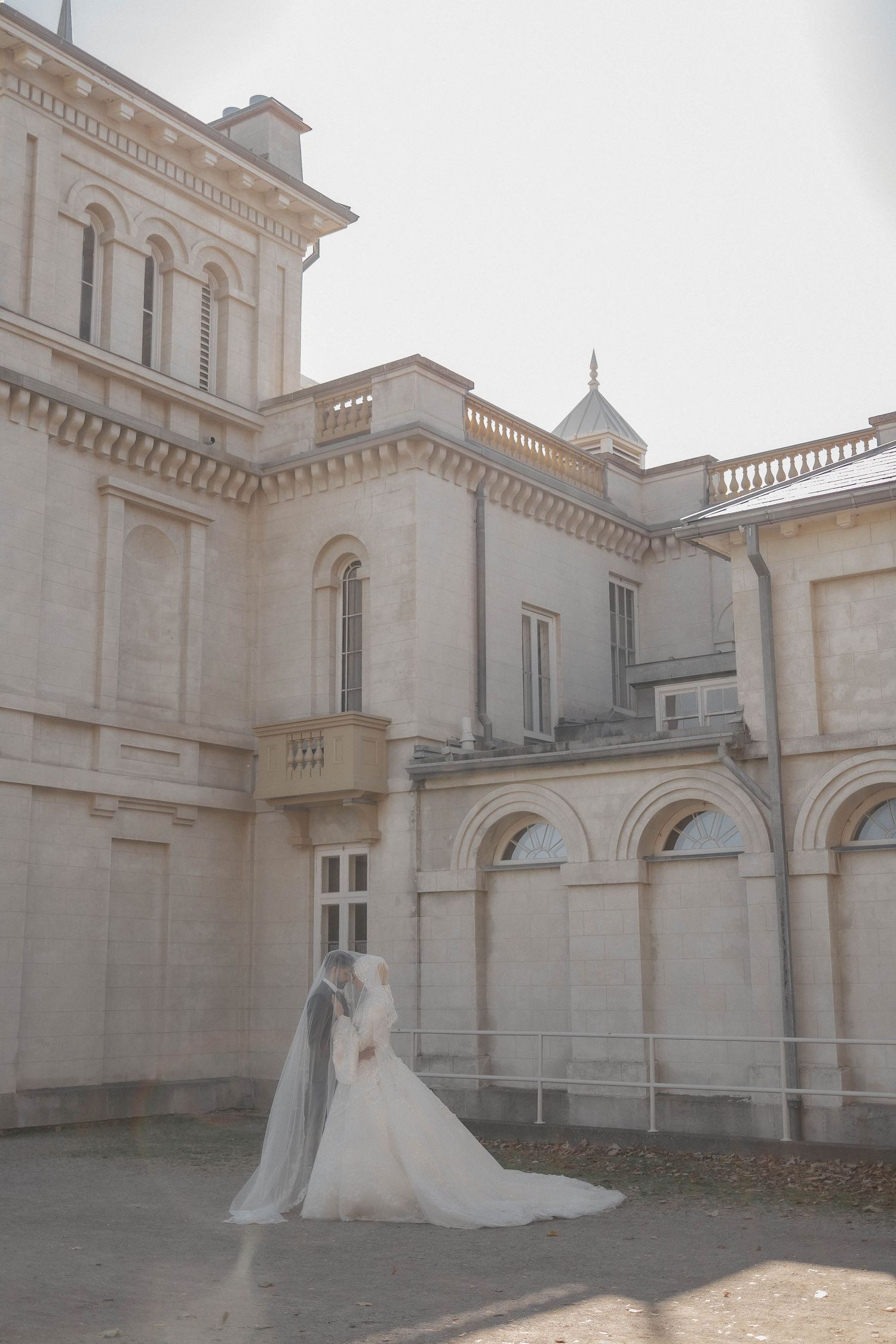Bride in flowing white dress standing outside elegant classical building architecture.