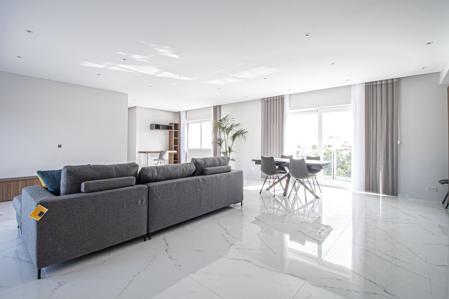 Modern spacious living room with grey sectional sofa, marble floors, and large windows.