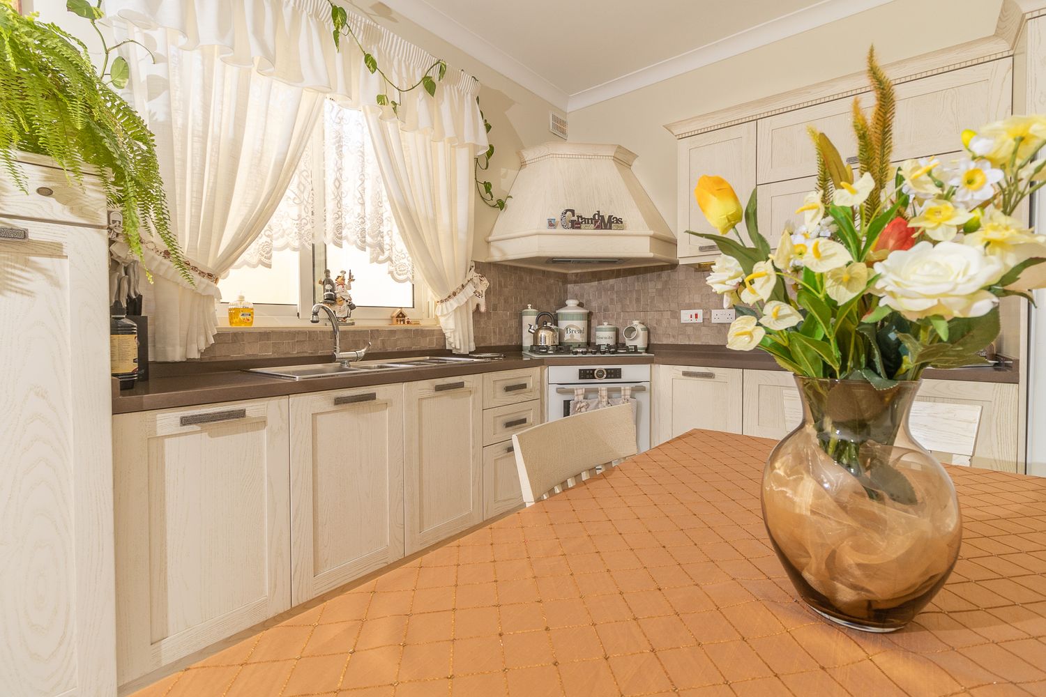 Elegant white kitchen with dark countertops, decorative hood, and fresh yellow flowers in a glass vase.